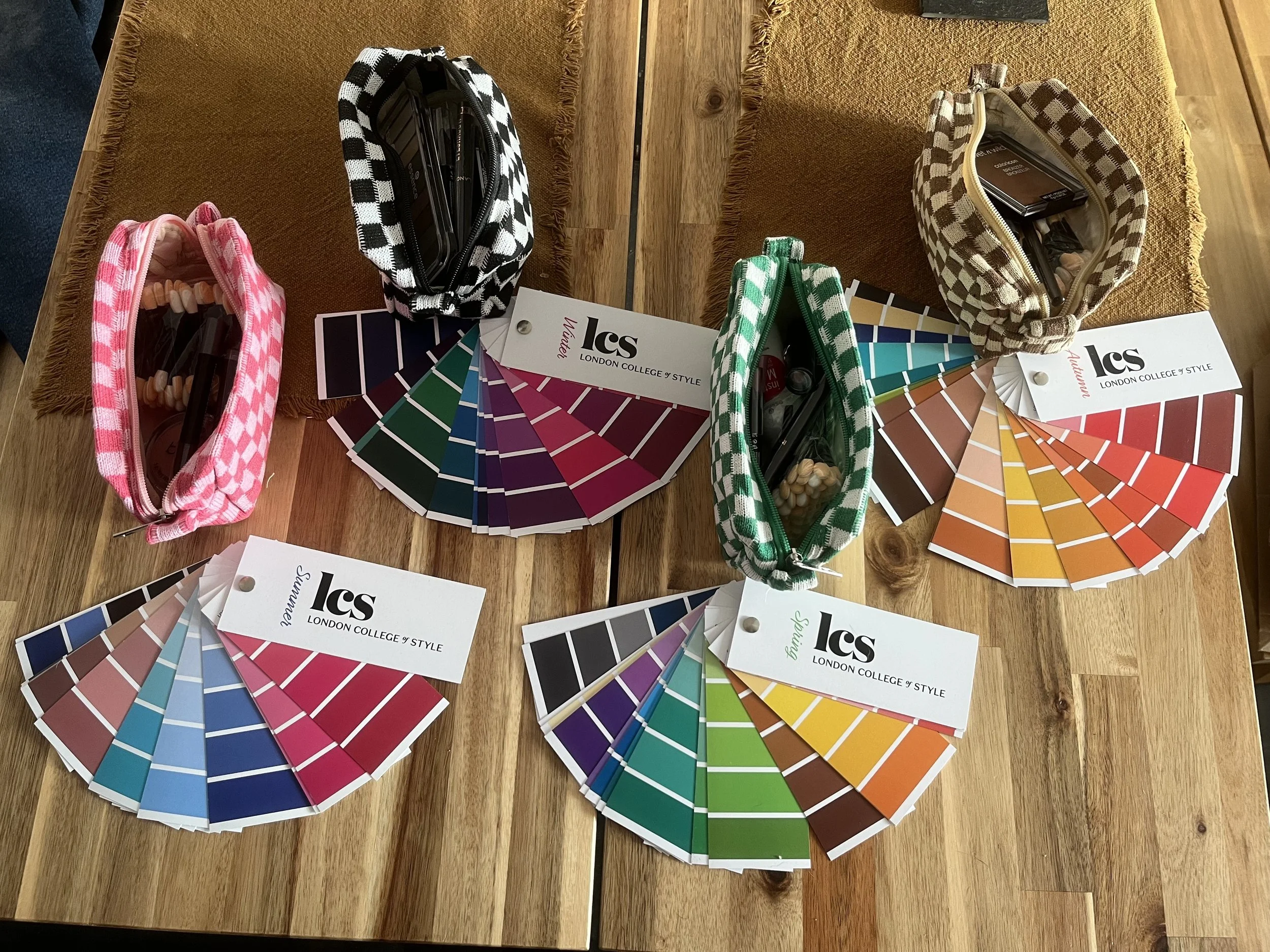 Color swatches of various shades arranged in fan shapes on a wooden table, with makeup brushes and samples in checked pouches, and LCS London College of Style tags.