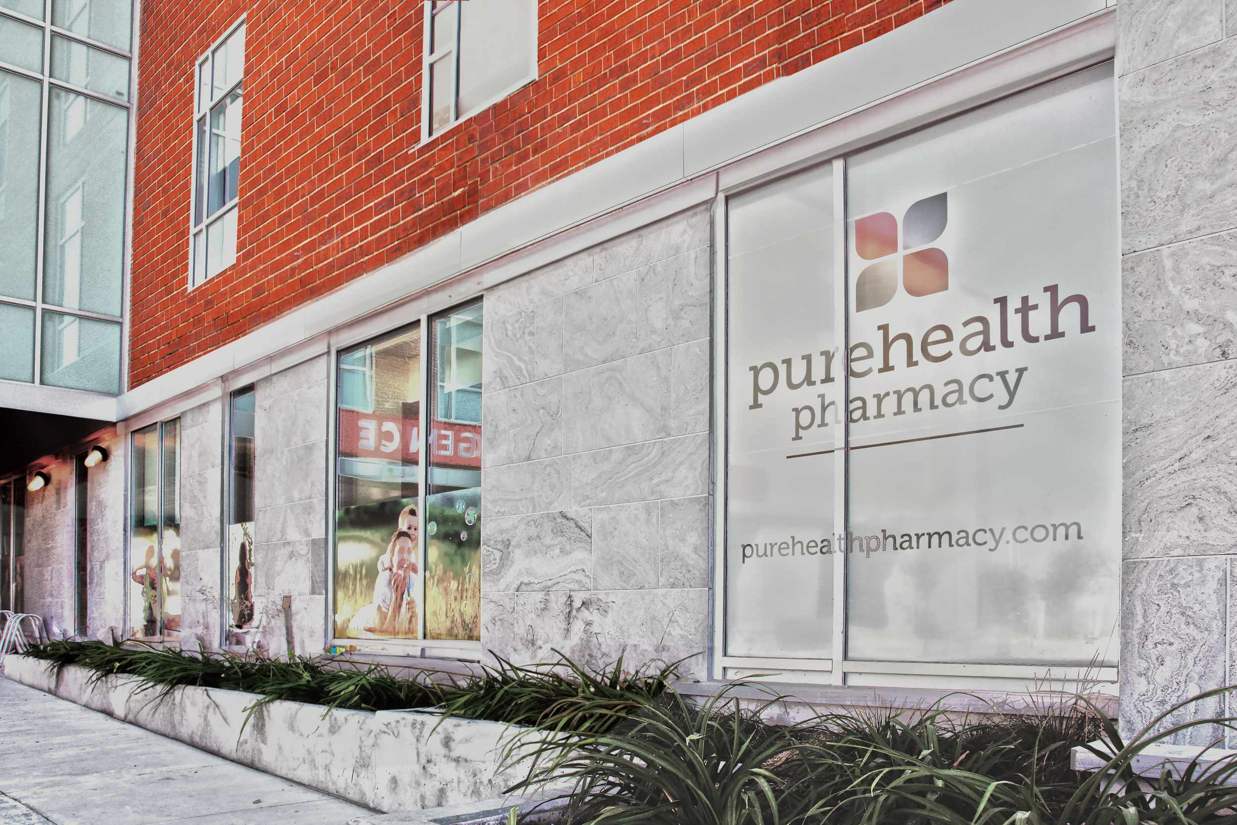 Exterior view of a building housing PureHealth Pharmacy, with glass windows, a brick wall, and a sign displaying the pharmacy's name and URL. healthcare, wellbeing. salutogenic design. wayfinding. Toronto, Dallas, Texas, Miami, and Park city.