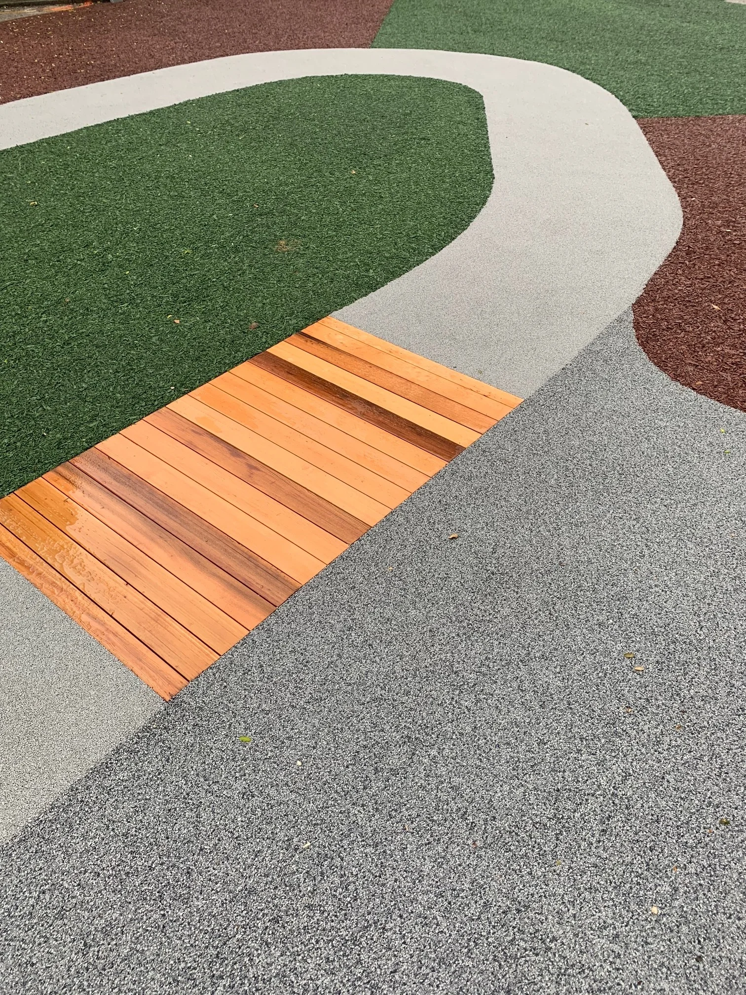 Close-up view of a sports field with multicolored synthetic running track, green turf, and wooden planks.  education, wellbeing. salutogenic design. wayfinding, human. inspiration for Toronto, Dallas, Texas, Miami, and Park City.