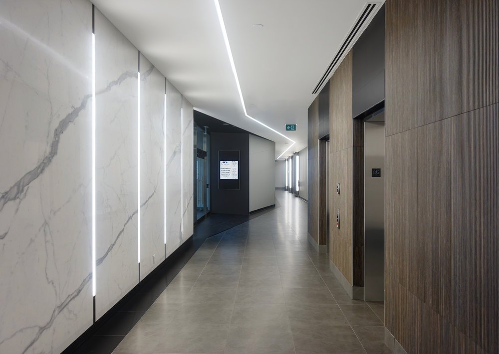 Modern hallway with marble and wood walls, elevator doors, digital directory, and ceiling lighting. easy wayfinding, helps with flow of patients and healthcare workers. Good inspiration for Toronto, Dallas and Park City.