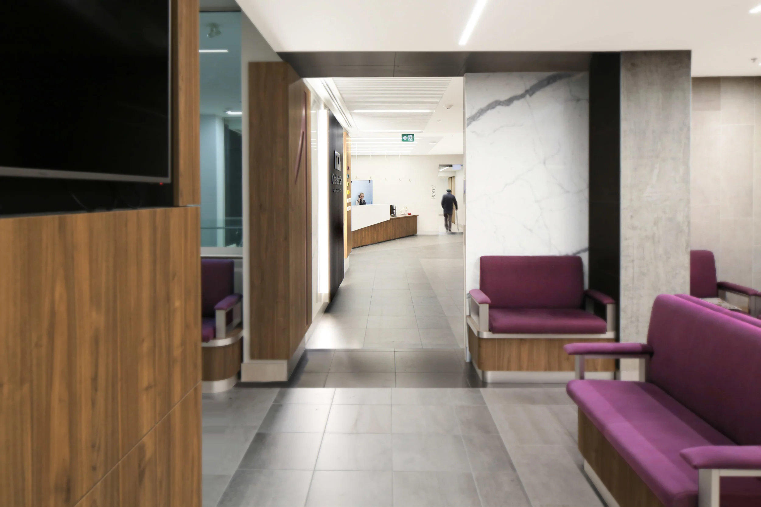 Interior of a modern waiting area with purple chairs, wooden partition, and a reception desk in the background. Wellbeing and flow, salutogenic design. Healthcare architecture. Good inspiration for Toronto, Dallas and Park City.