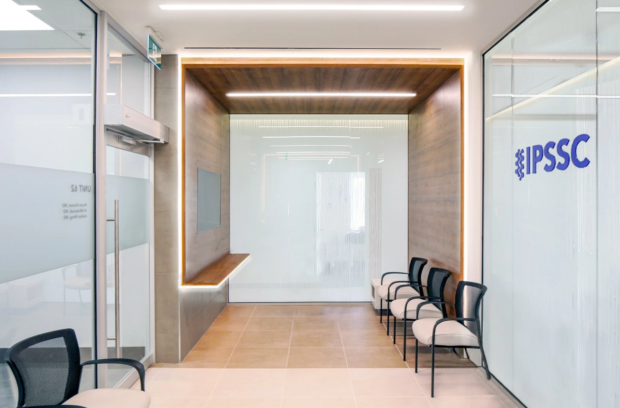 Modern office waiting area with black chairs and white cushions, glass walls with branding for IPSSC, wooden accents, and bright lighting. Healthcare architecture inspiration for Toronto, Dallas and Park City.
