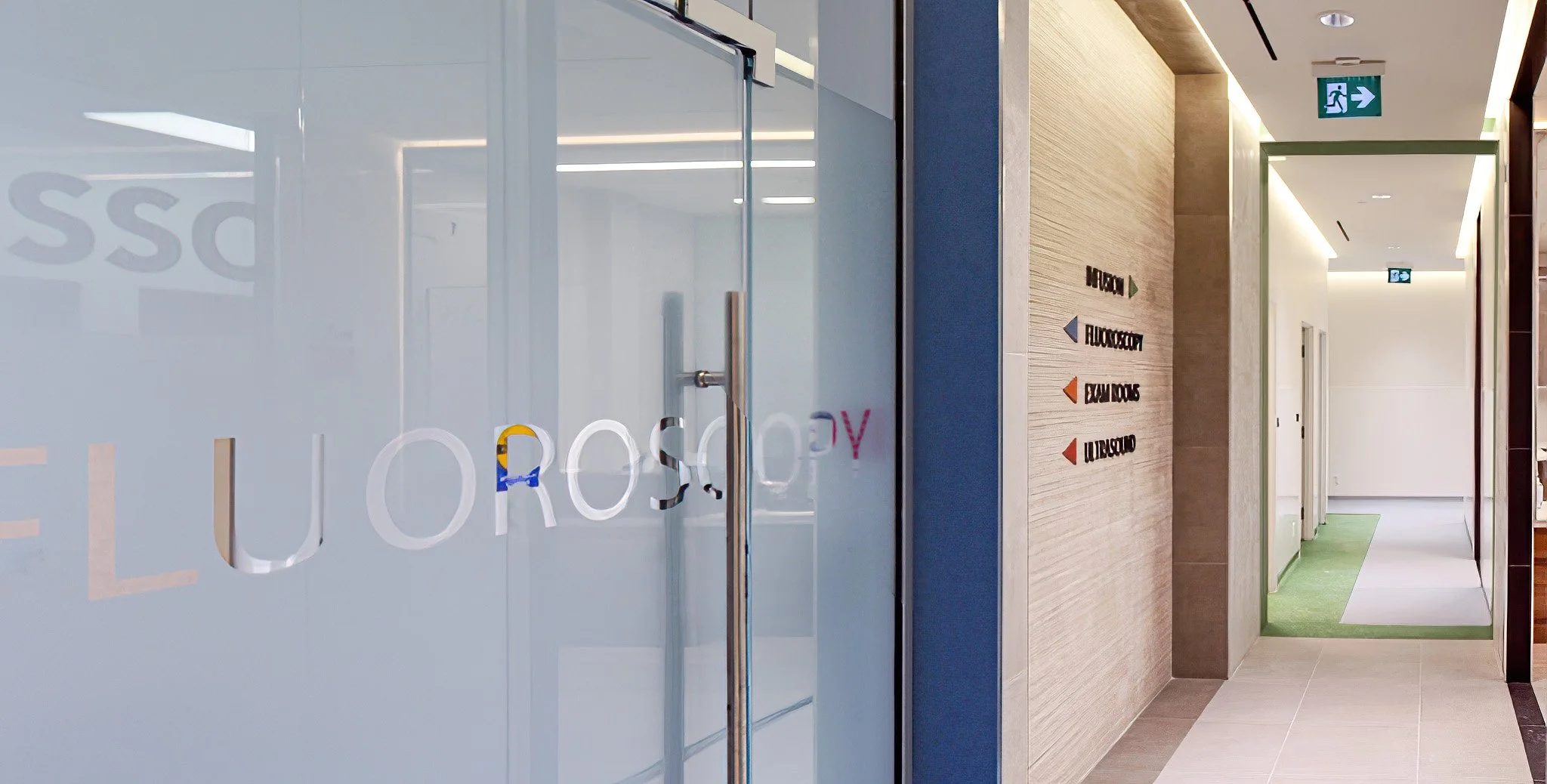 Modern office hallway with a glass door and a directory on the wall, featuring colored arrows and office room labels. Healthcare architecture that promotes wellbeing and easier wayfinding. Inspiration for Toronto, Dallas and Park City.