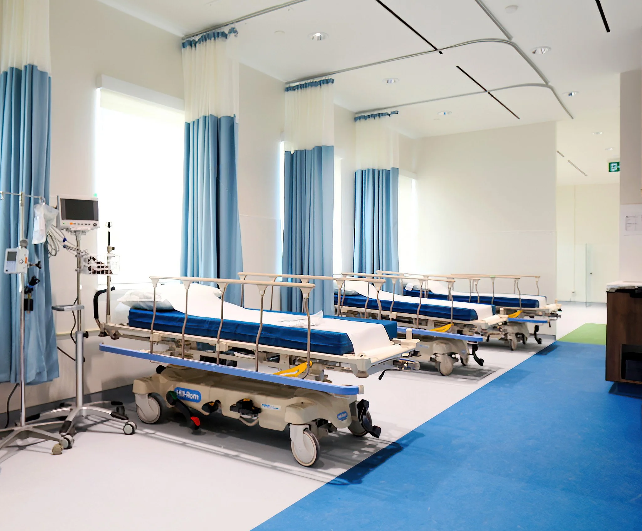 Empty hospital room with two hospital beds, medical equipment, and curtains, brightly lit with large windows. Healthcare architecture that promotes wellbeing and easier wayfinding. Inspiration for Toronto, Dallas and Park City.