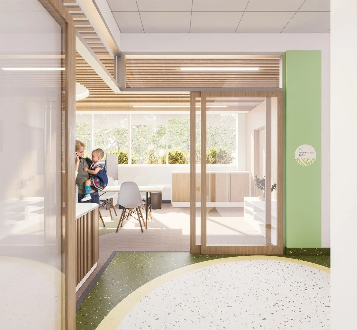 A bright, modern family resource center with a glass door entrance. Inside, there is a small seating area with a table and chairs. The room features natural light, with large windows and a ceiling with wooden slats. Toronto, Dallas, Park city.