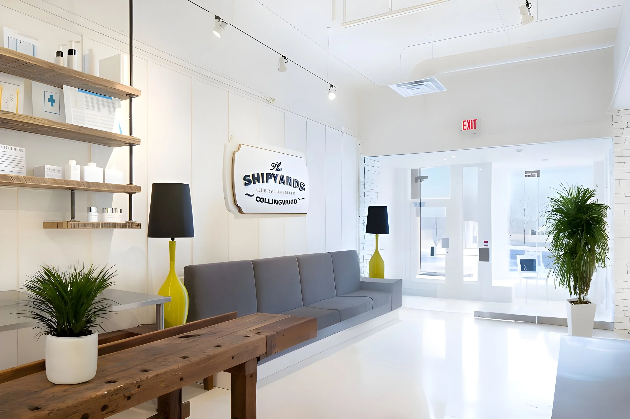 Modern, bright interior space with white walls and high ceilings, decorated with potted plants, yellow lamps, and wooden furniture, including a long wooden table and a gray sofa. Shelves with bottles and containers are on the left, and a sign reads '