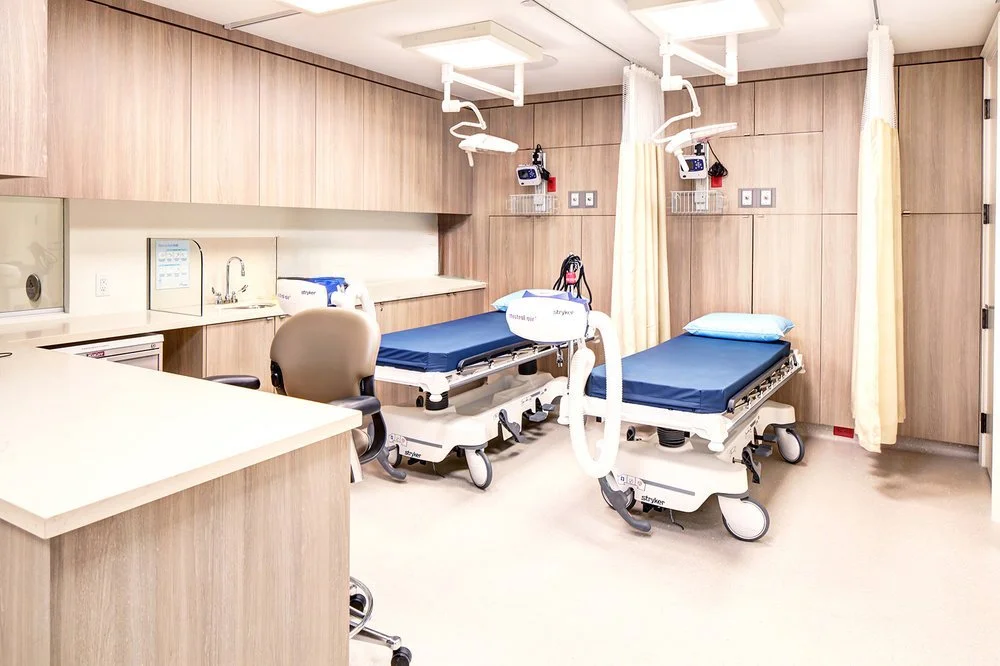 Hospital room with two patient beds, medical equipment, curtains, and a chair.