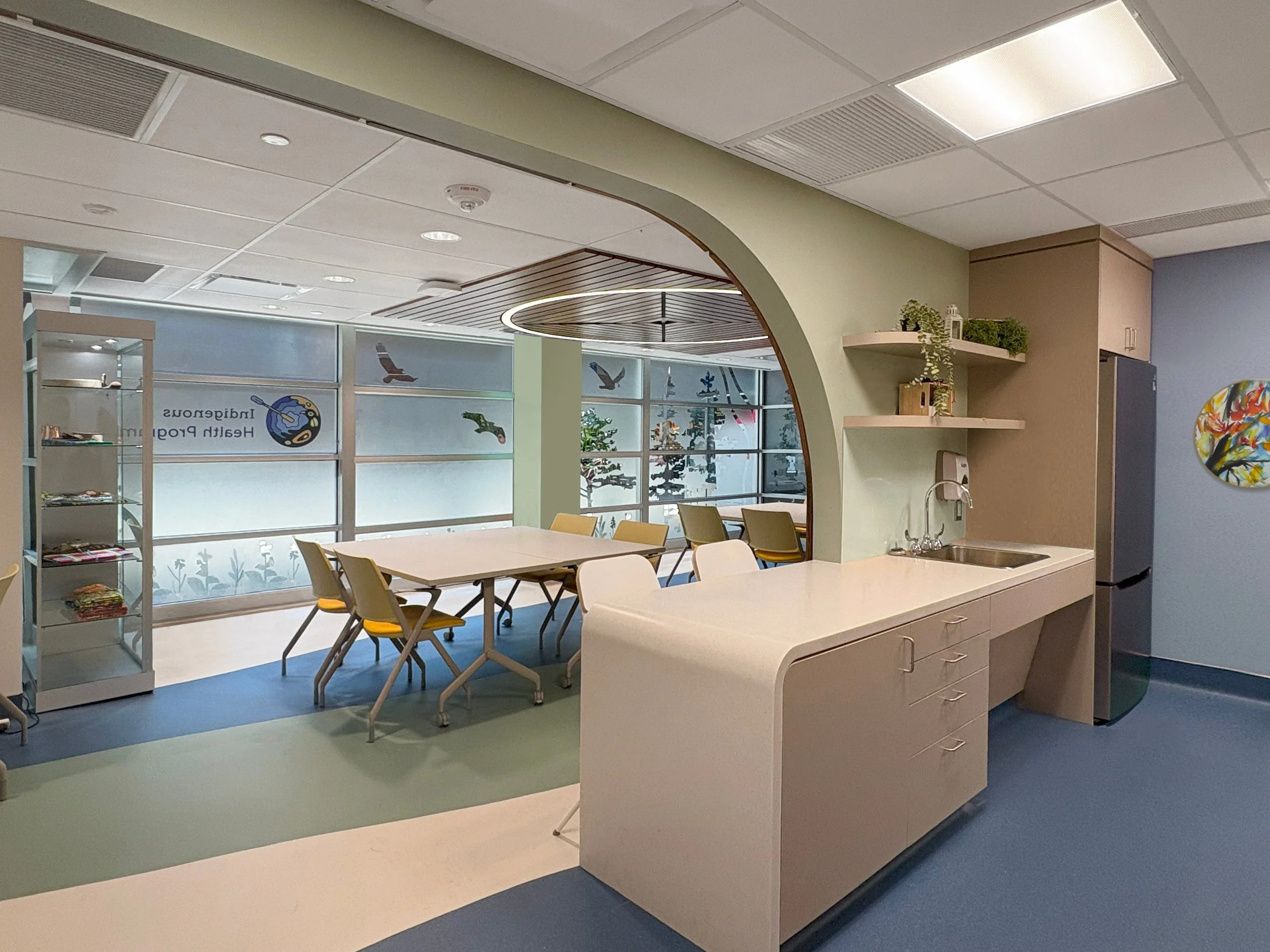 Interior of a modern medical or office space with a seating area, a counter with a sink, and windows decorated with airplane and dinosaur stickers.