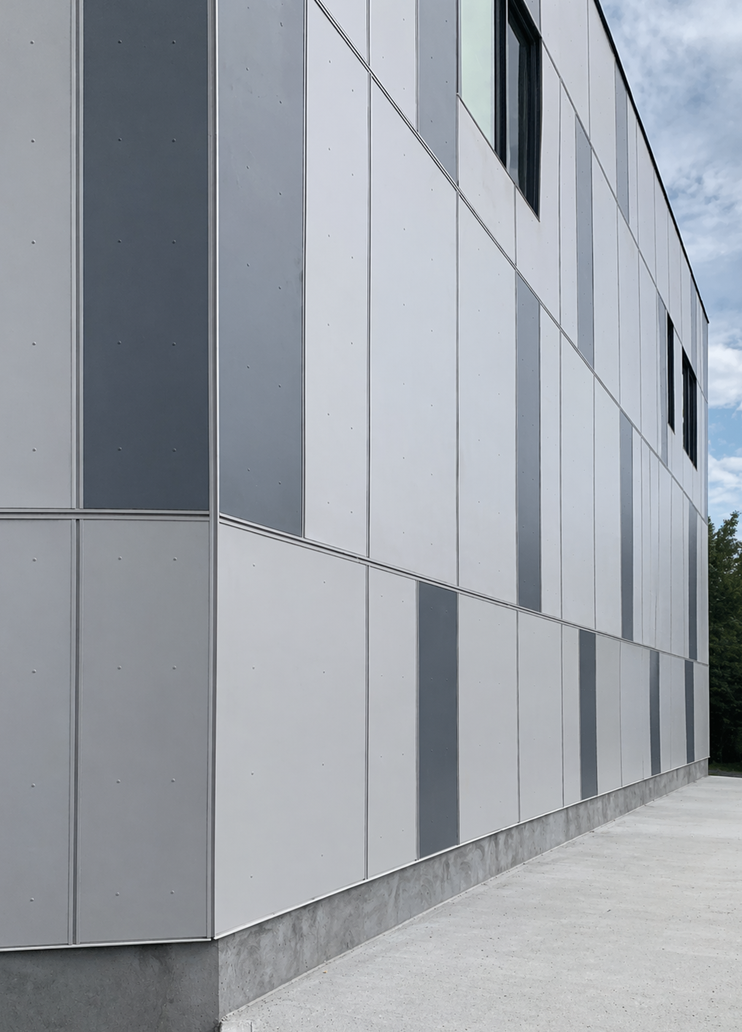 Modern building with metallic exterior panels and windows, concrete sidewalk in front, under cloudy sky. Healthcare architecture that promotes wellbeing and easier wayfinding. Inspiration for Toronto, Dallas and Park City.