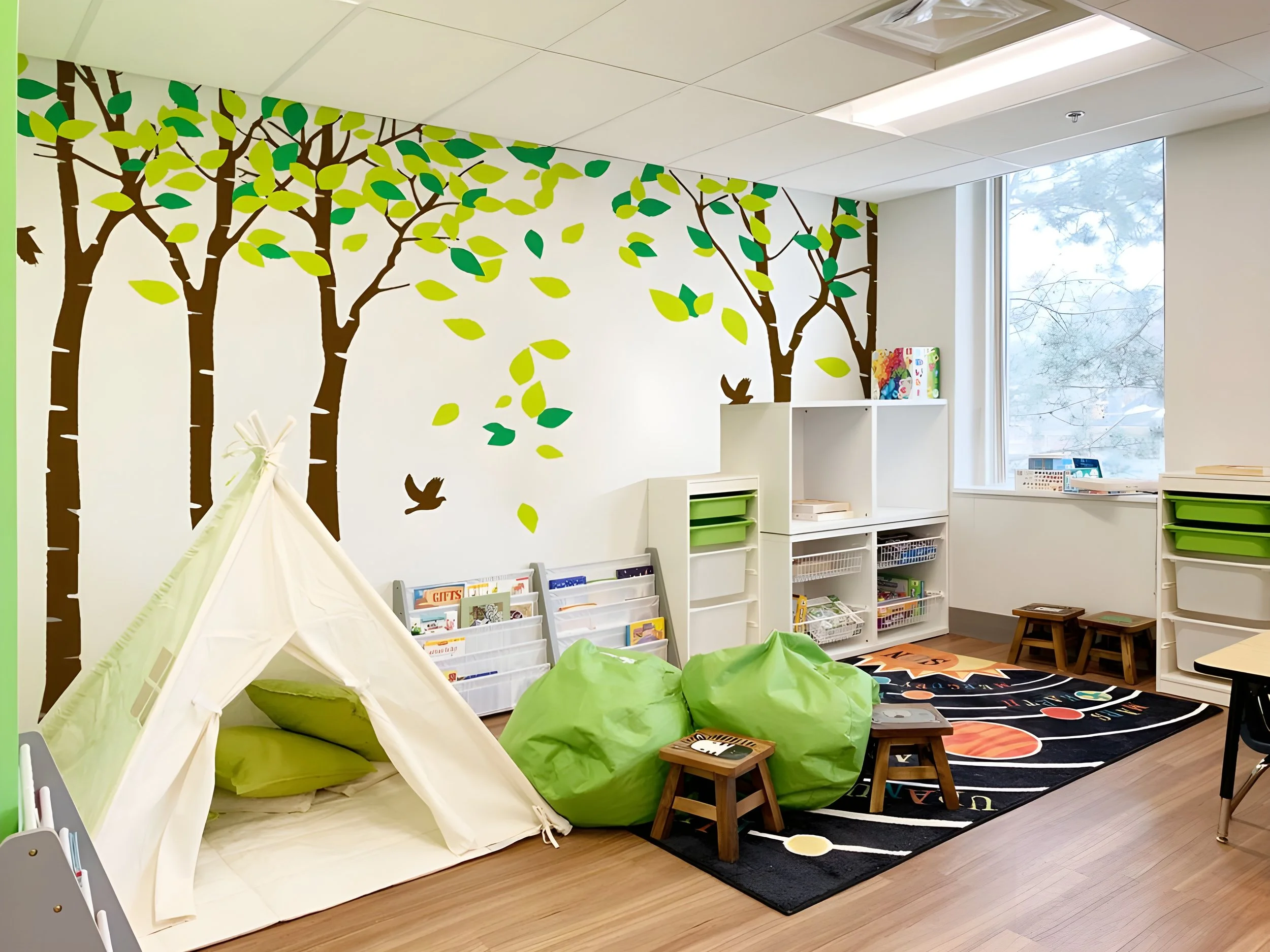 A room with a tree mural on the wall, a white bookshelf with green bins, a black and orange rug, and a white teepee tent with green bean bags nearby. There are small stools and a table with books and toys, and large windows letting in natural light.
