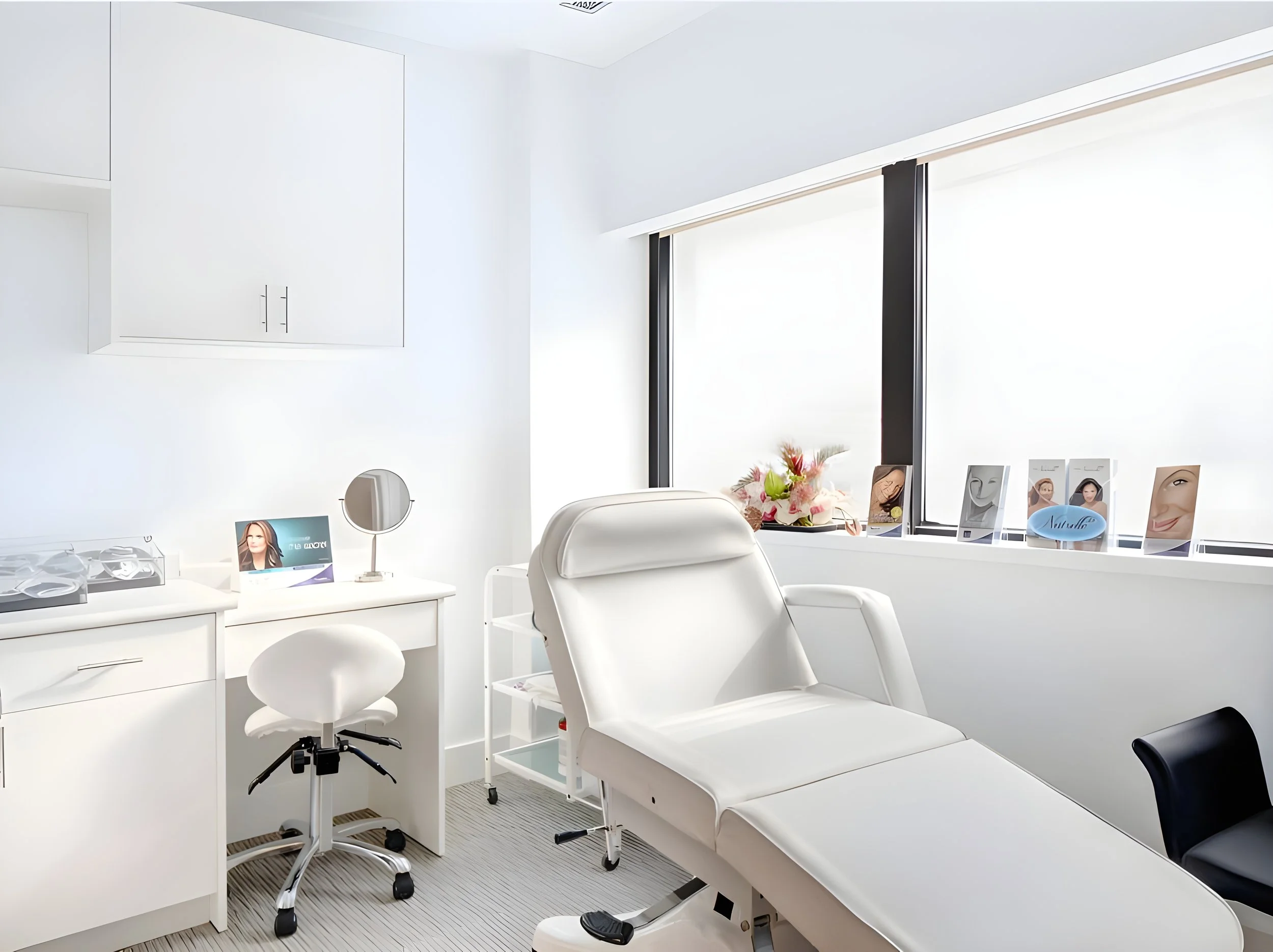 A modern, bright white medical or spa treatment room with a reclining chair, additional chairs, a small table, and various beauty or skincare product displays near the window. Healthcare. Inspiration for Toronto, Dallas, Texas, Miami and Park city.