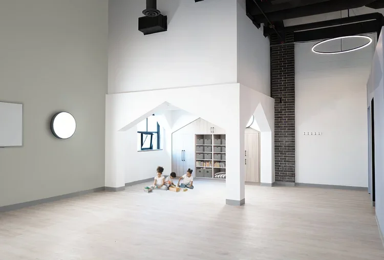 Two children sitting on the floor playing with toys in a modern, minimalist room with white walls and light hardwood flooring.
