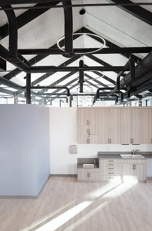 Modern industrial-style kitchen with exposed black ductwork and a circular LED light on a high vaulted ceiling.