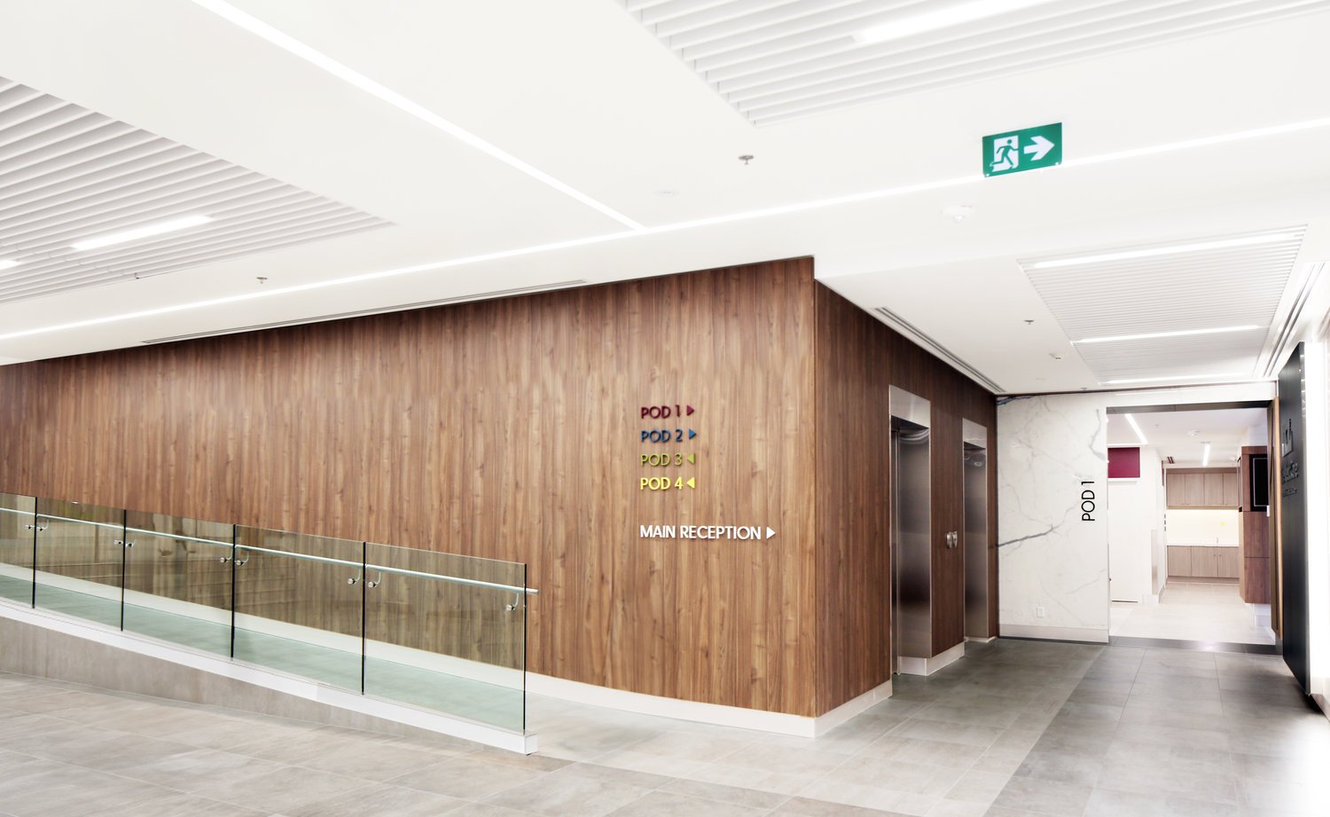  Interior view of a modern building with elevator doors, wooden wall, and directional signs for POD rooms and main reception, along with an emergency exit sign. Promotes wellbeing and wayfinding. Good inspiration for Toronto, Dallas and Park City.