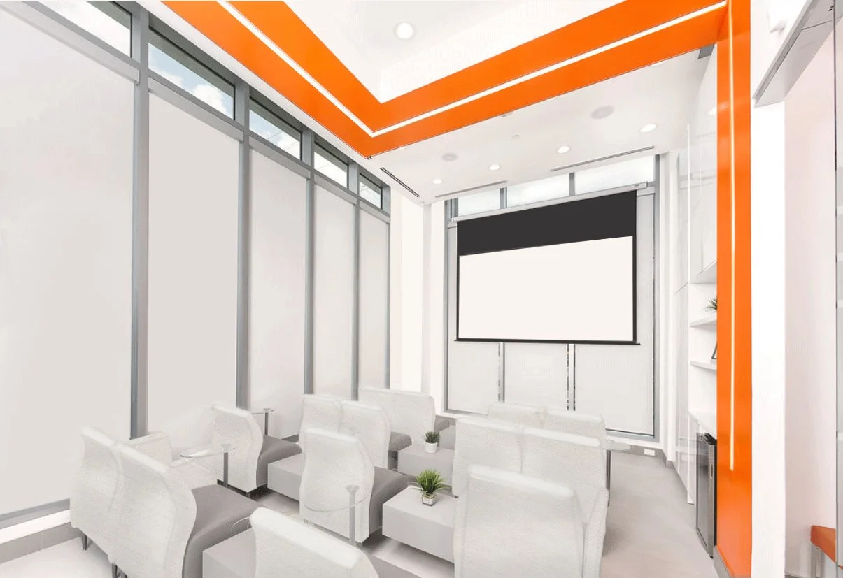 Modern conference or presentation room with white chairs arranged in a semi-circle, a large projection screen, and orange accents on the ceiling and walls.