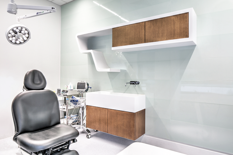 An examination room in a medical facility with a black office chair, medical equipment, and modern cabinetry on a mint green wall.  healthcare, wellbeing. salutogenic design. wayfinding. inspiration for Toronto, Dallas, Texas, Miami, and Park city.