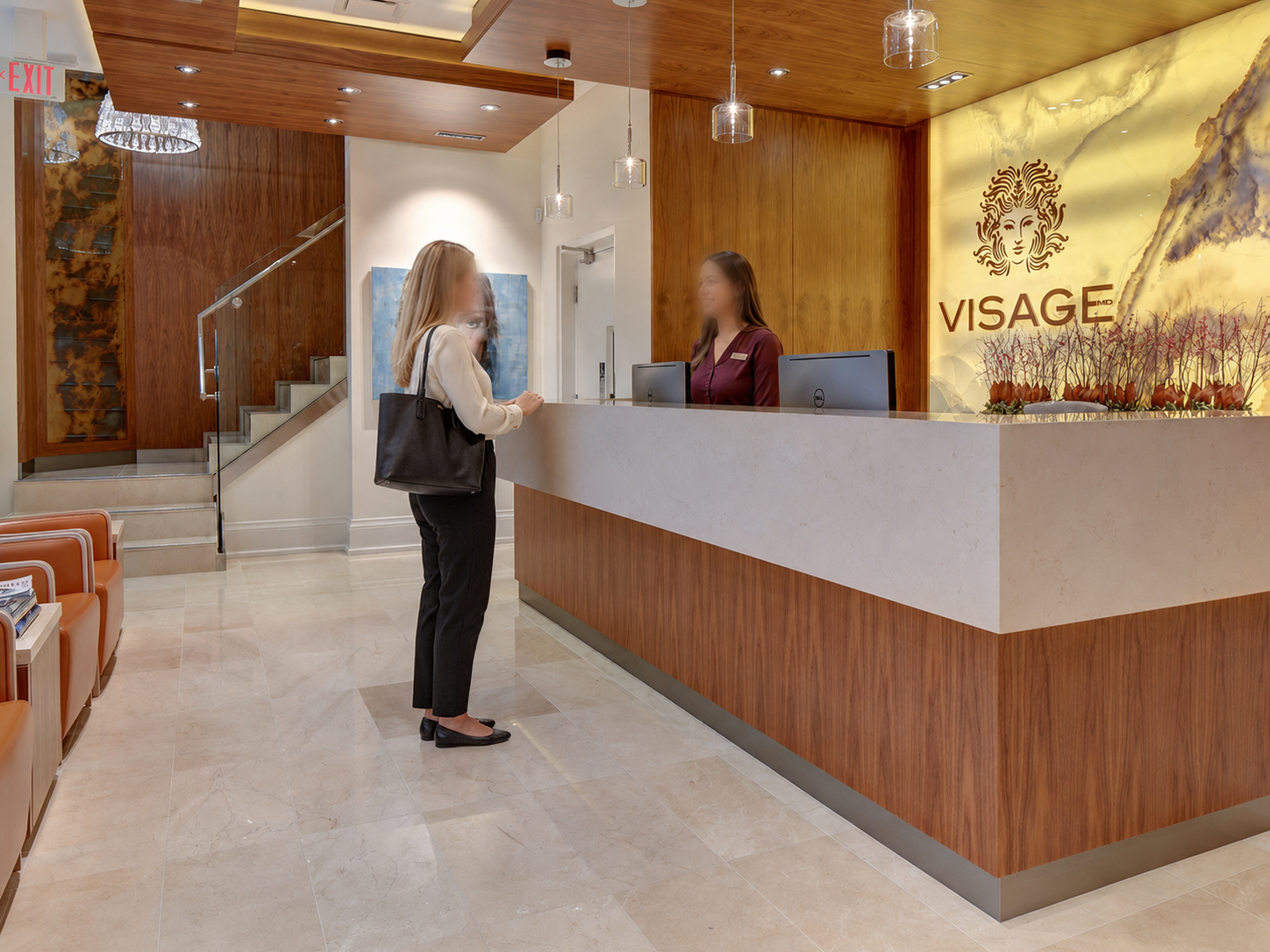Hospital or clinic reception area with wooden walls, a white counter, and decorative lighting. There is a portrait of a woman on the wall, a large illuminated logo that reads 'VISAJE' with a lion's face, and a large flower arrangement.