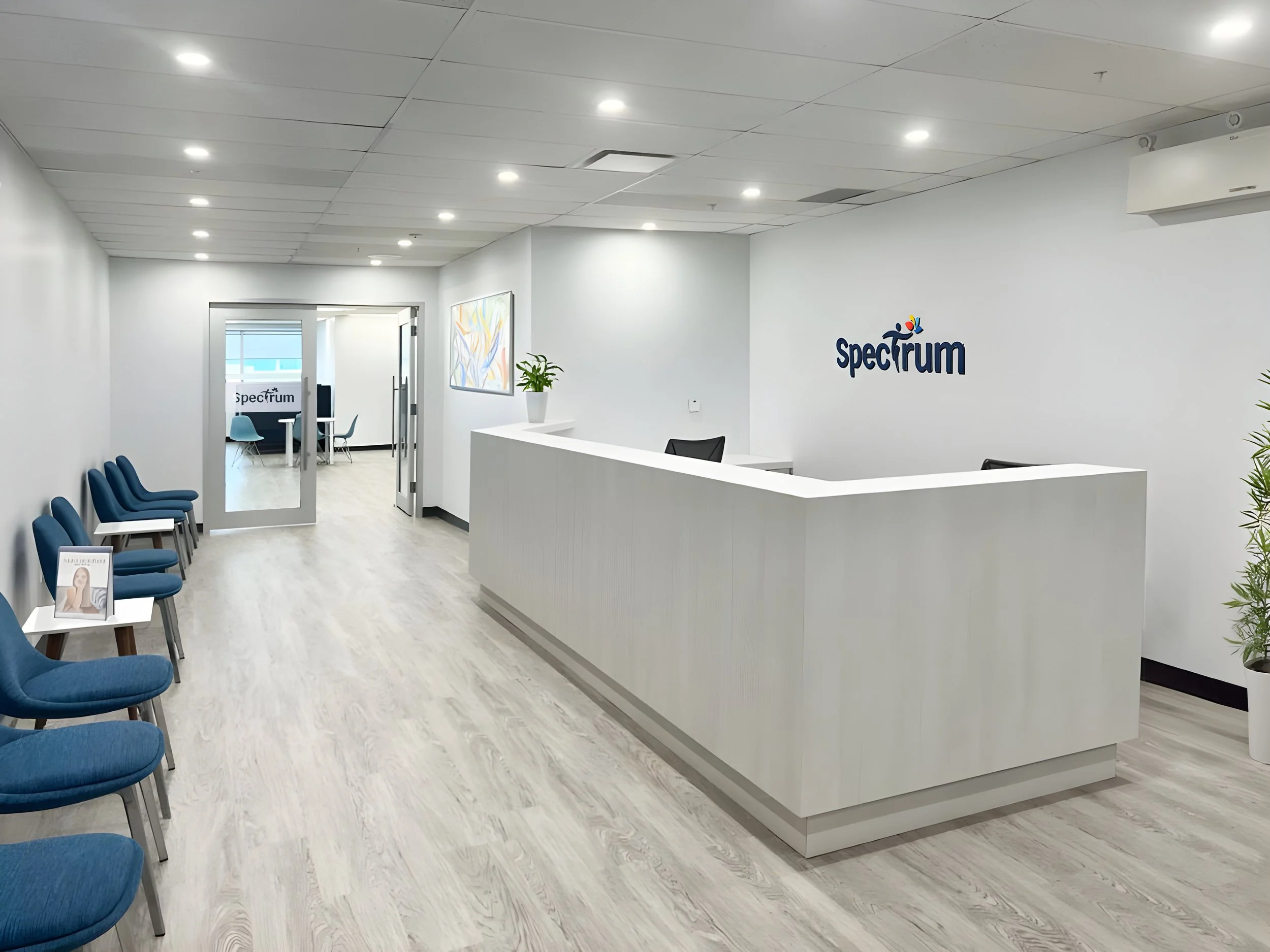 Modern reception area with white walls, blue chairs, white reception desk, and a Spectrum logo on the wall. Education architecture. wellbeing. salutogenic design. Inspiration for Toronto, Dallas, Texas, Miami, and Park city.