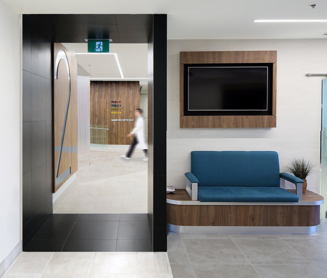 Modern hotel lobby with an elevator, a seating area with a blue sofa, wall-mounted television, and sign indicating the main reception and pod areas. Healthcare, salutogenic design, flow. Good inspiration for Toronto, Dallas and Park City.