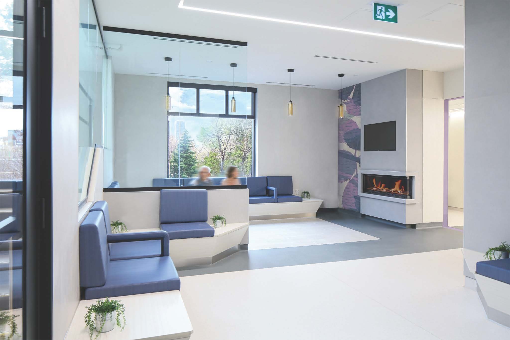 Modern lobby area with blue cushioned seating, large window showing outside trees, a fireplace, and decorative plants. Promotes salutogenic design and easy wayfinding due to good flow. Good inspiration for Toronto, Dallas and Park City.