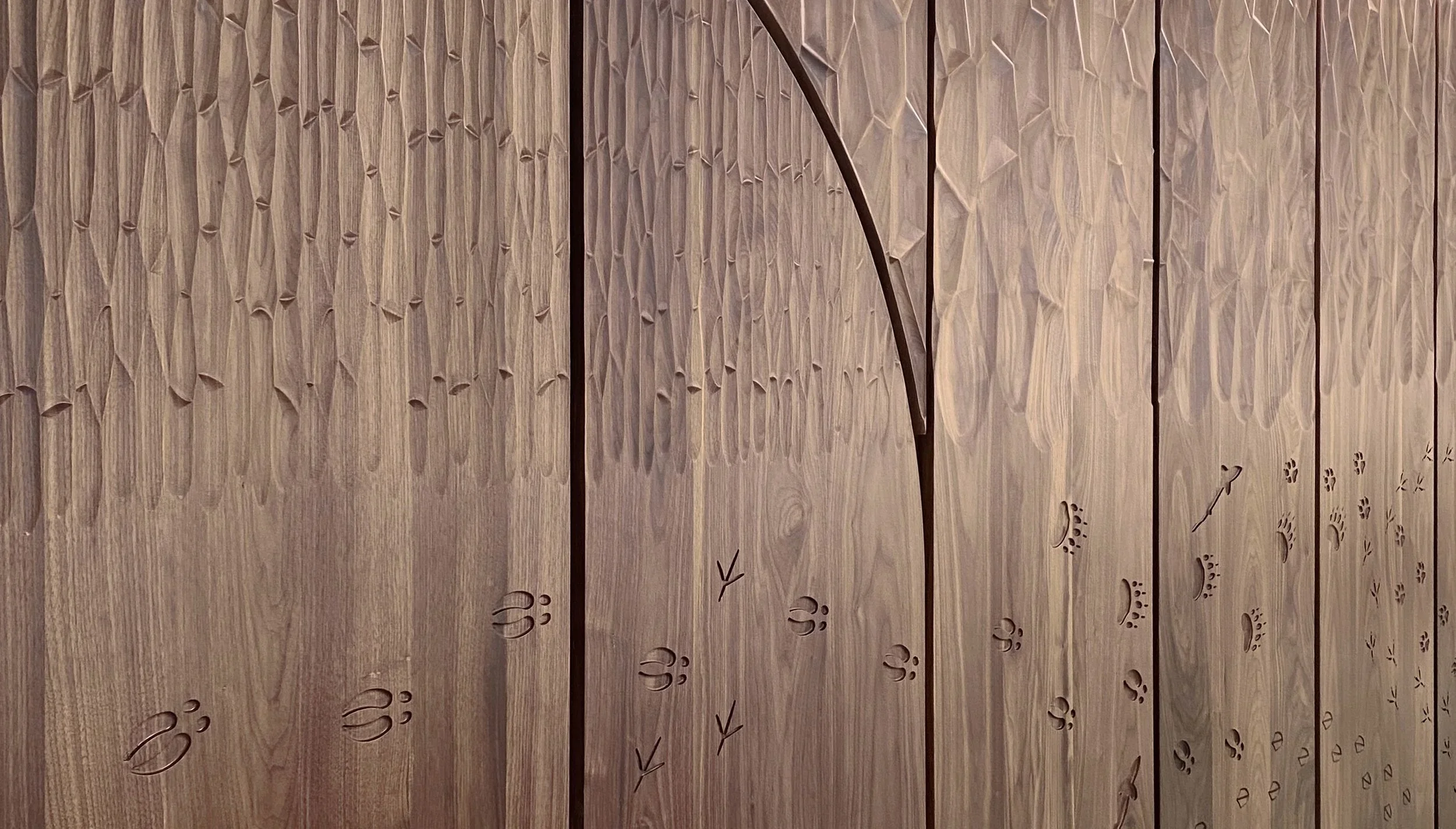 Wooden wall with carved animal paw prints, arrows, and geometric patterns.