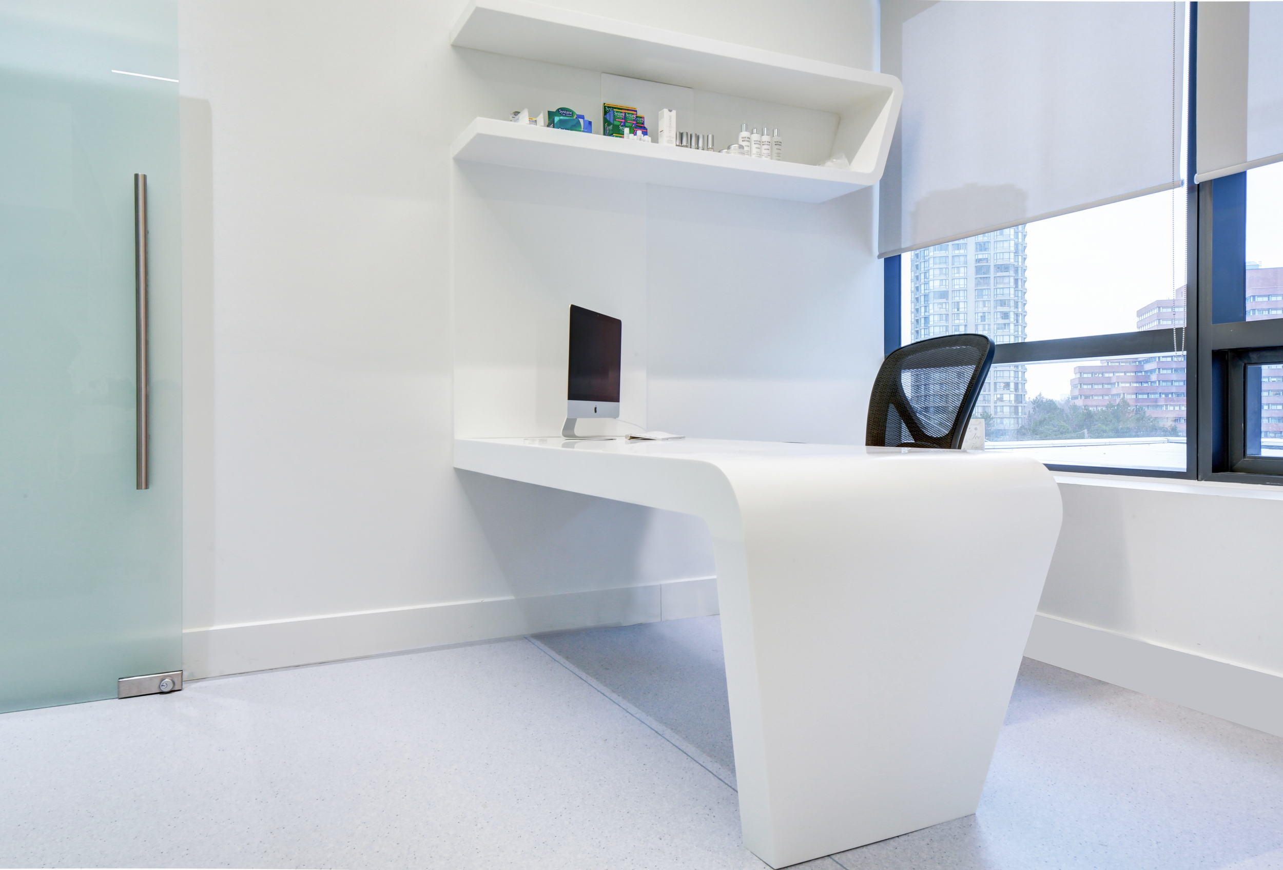Modern office reception area with a white curved desk, black office chair, and a large window showing high-rise buildings outside.  healthcare, wellbeing. salutogenic design. wayfinding. inspiration for Toronto, Dallas, Texas, Miami, and Park city.