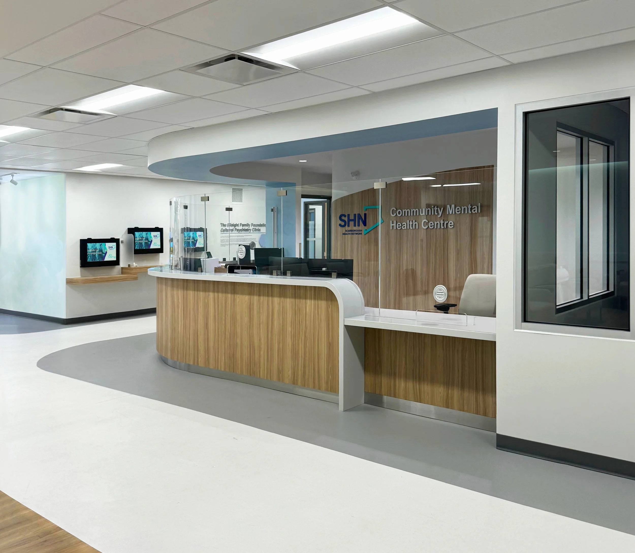 Interior of a community mental health center with a reception desk, glass partitions, and digital screens, featuring a sign that reads 'Community Mental Health Centre.'