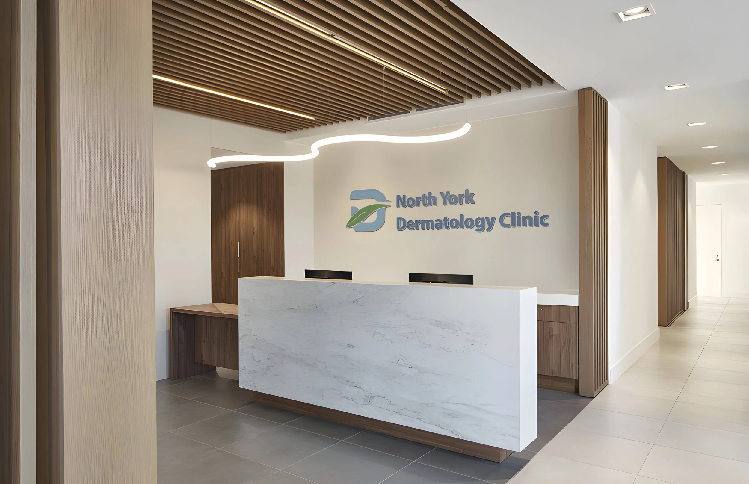 Reception area of North York Dermatology Clinic with a white marble counter, wood accents, and a modern curved light fixture. Healthcare architecture that promotes wellbeing and easier wayfinding. Inspiration for Toronto, Dallas and Park City.