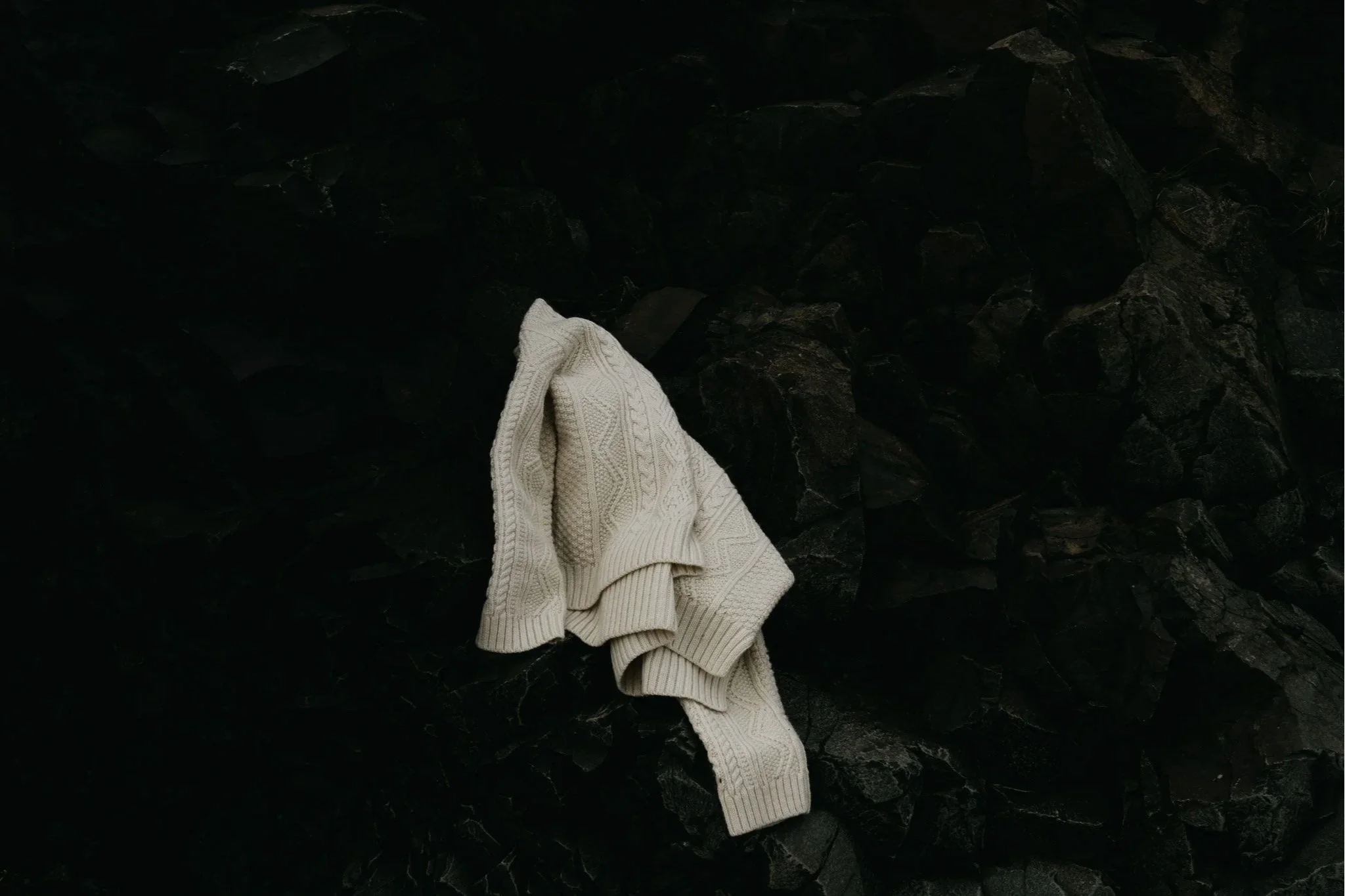 An Idris wool sweater made by OUBAS Knitwear draped over volcanic rocks in Iceland creating an impactful, contrast-rich product image