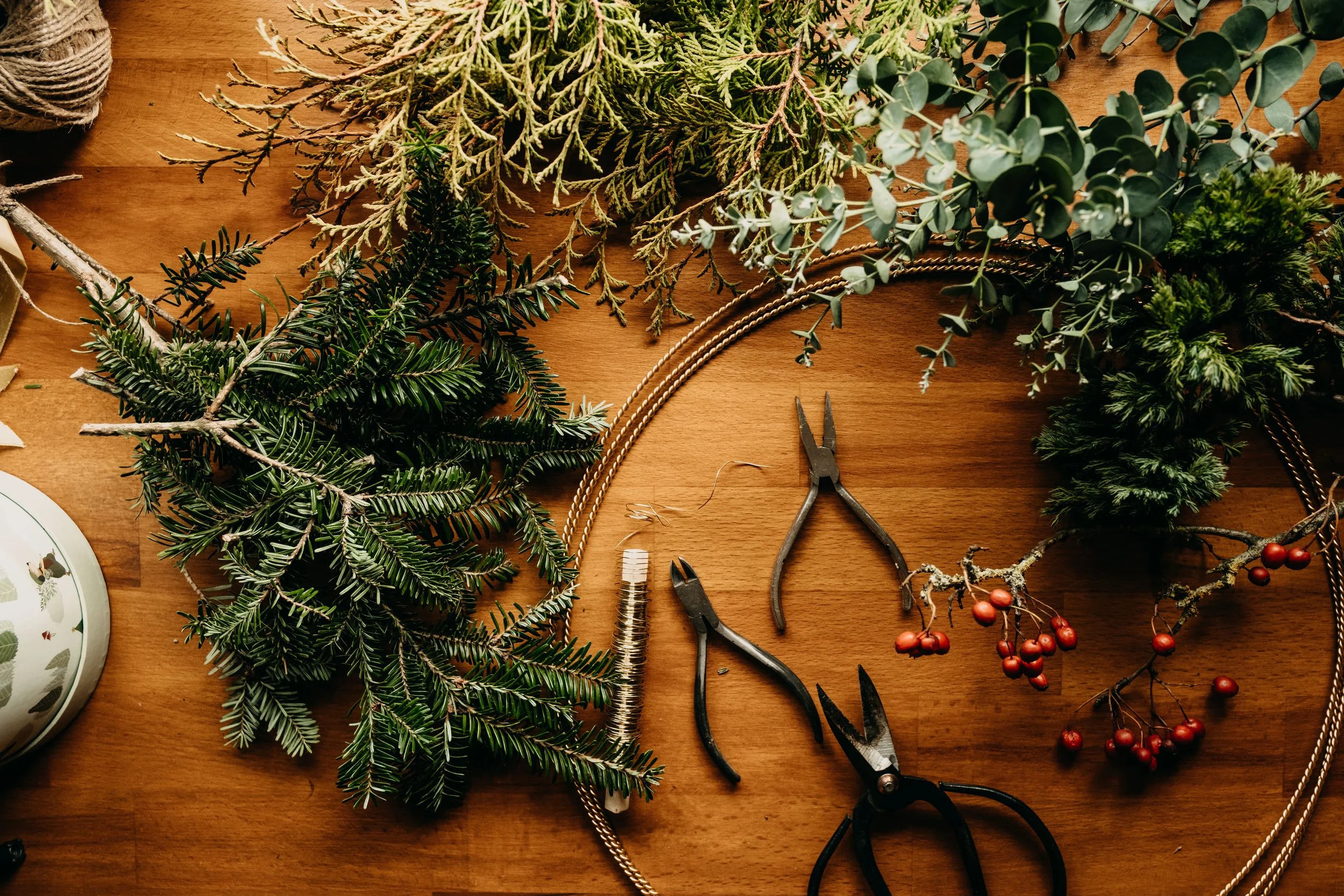 Flatlay photo of a rustic table covered with Christmas wreath making supplies and foraged evergreens and foliage