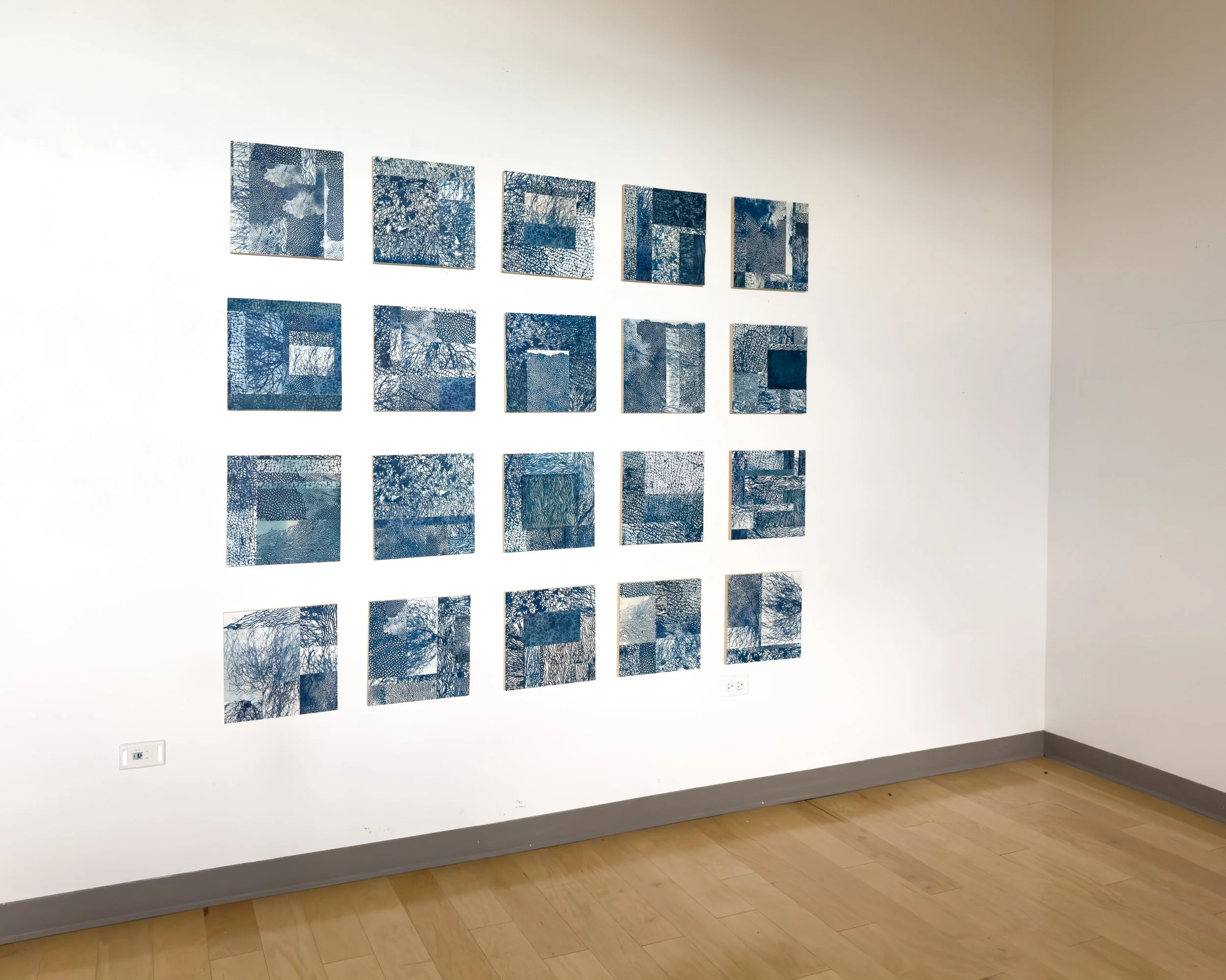 Gallery wall with multiple abstract blue geometric artworks in a white-walled room.
