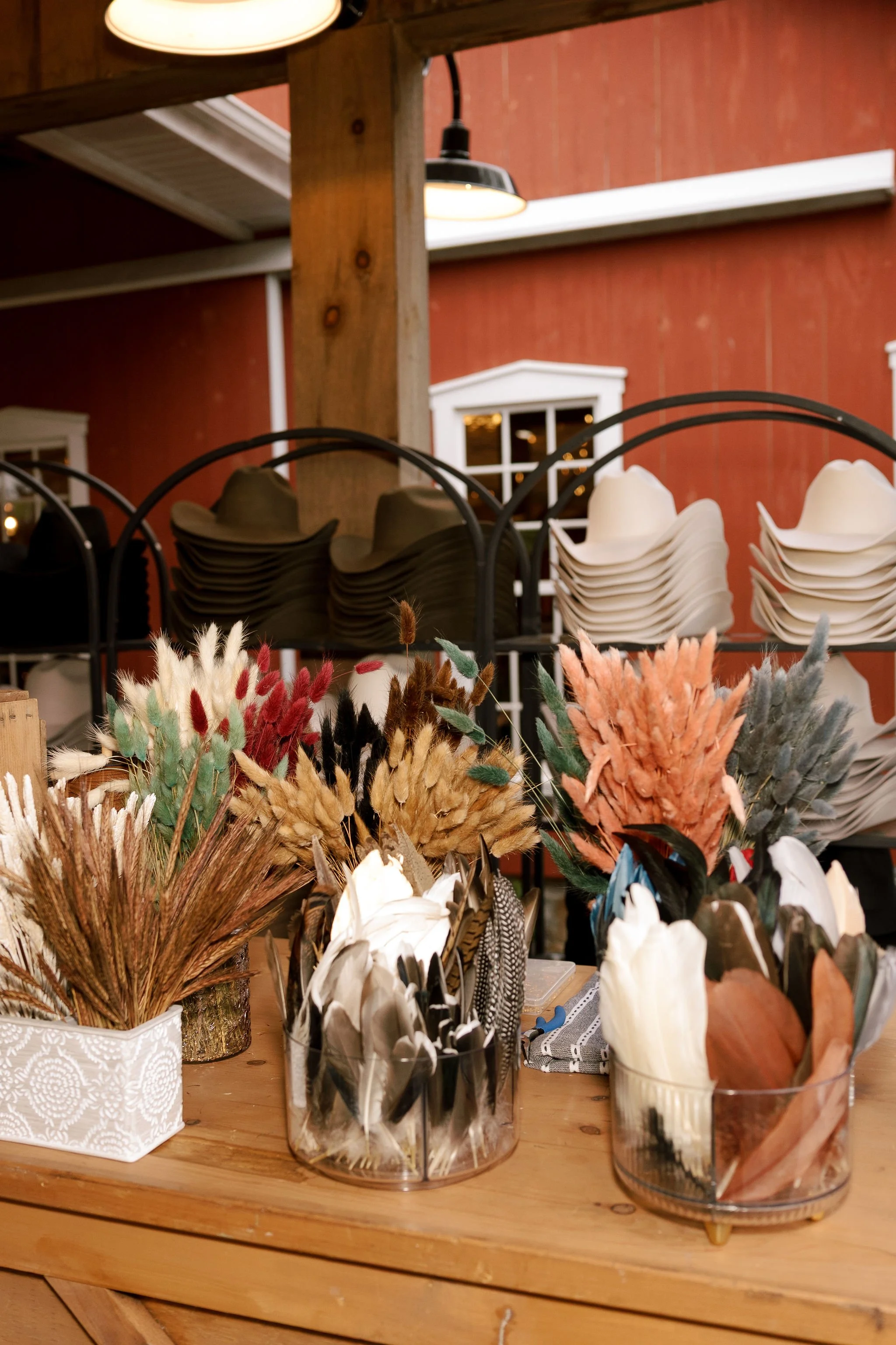 A display of assorted dried and preserved flowers in glass vases and containers on a wooden table, for a fun custom hat station at a Lizzie Noble Events wedding.