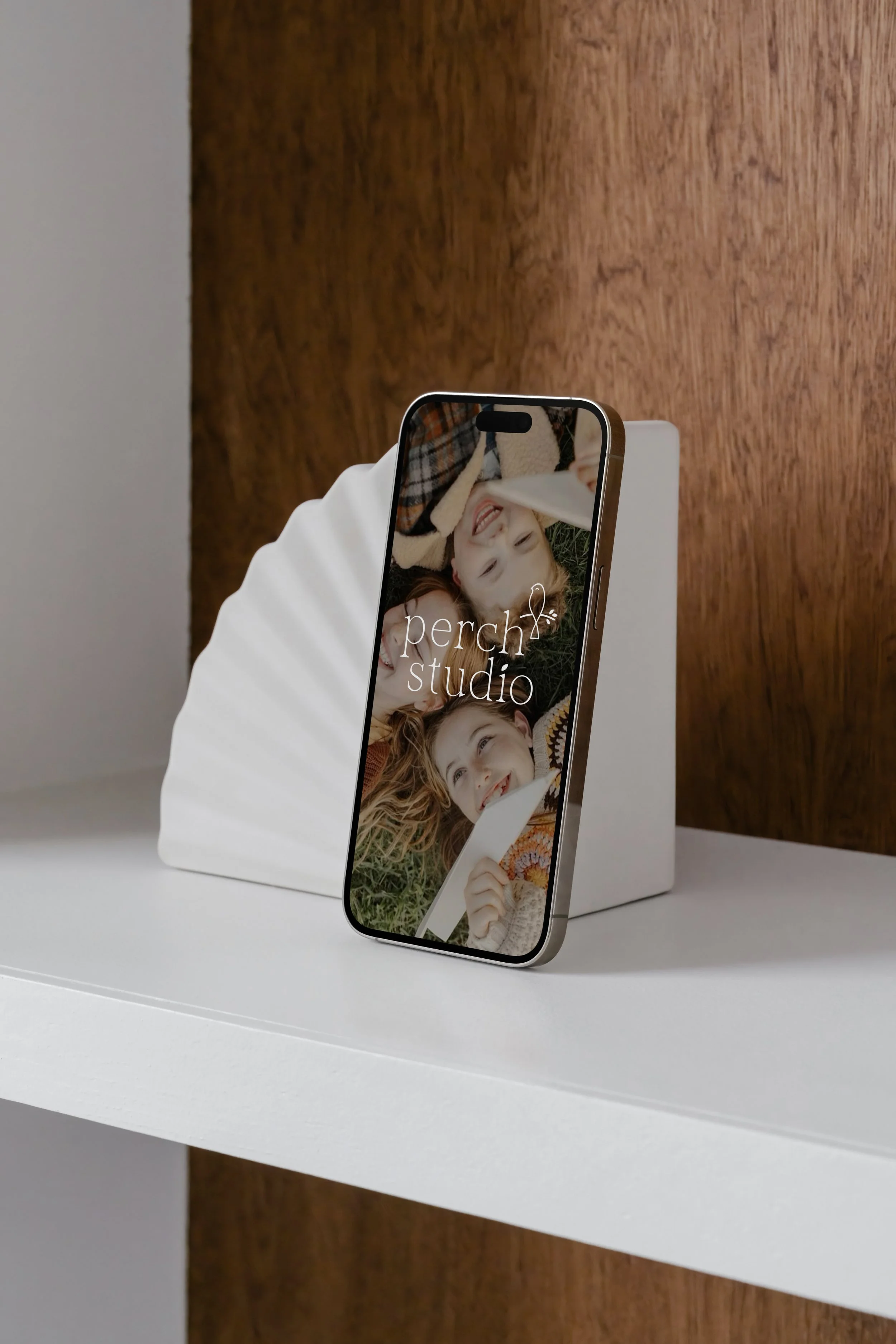 Smartphone displaying the Perch Studio family photography website, propped against a white tablet on a desk