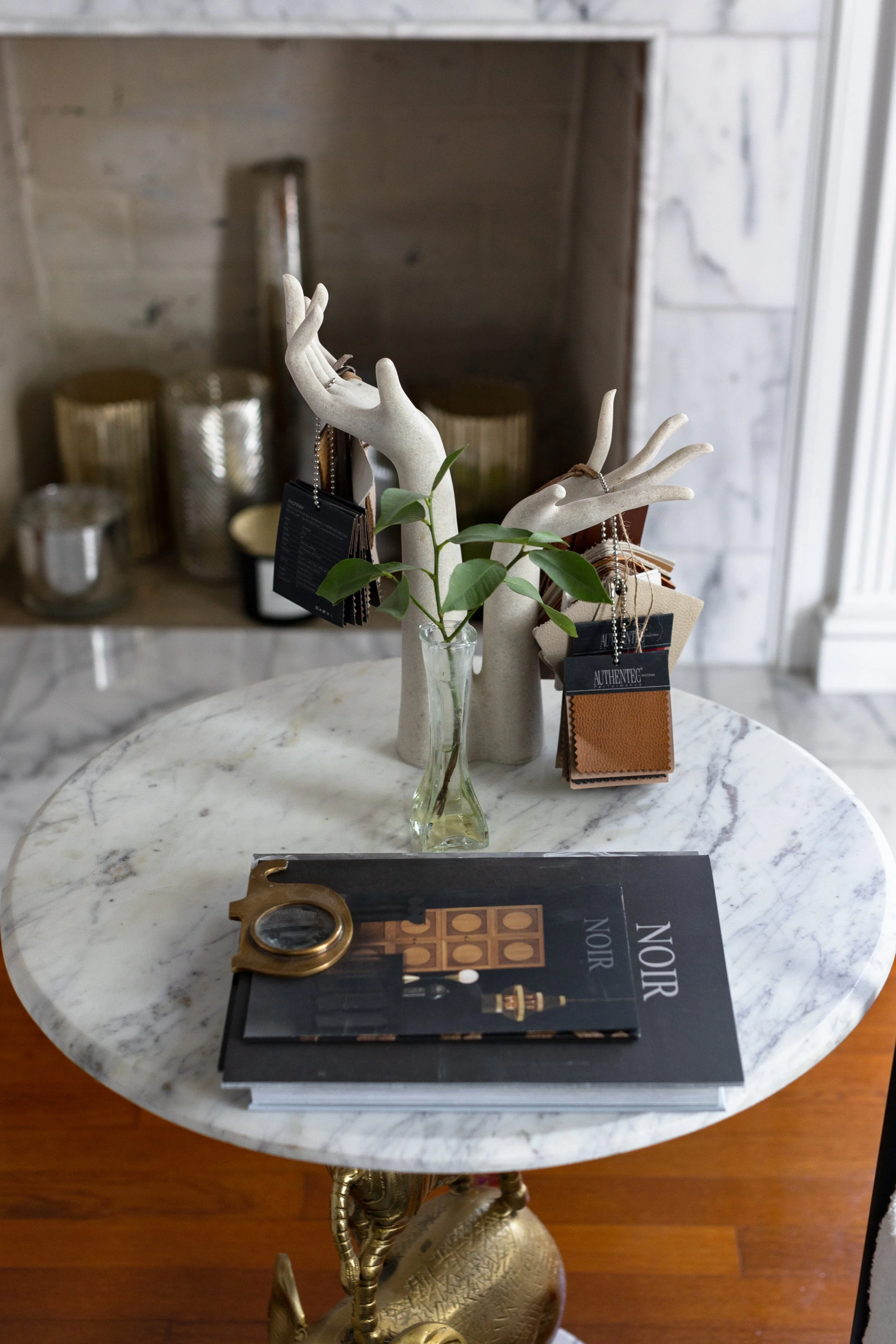 Decorative round marble table with jewelry display, a small open book, and a glass vase with green leaves, in a stylish interior.