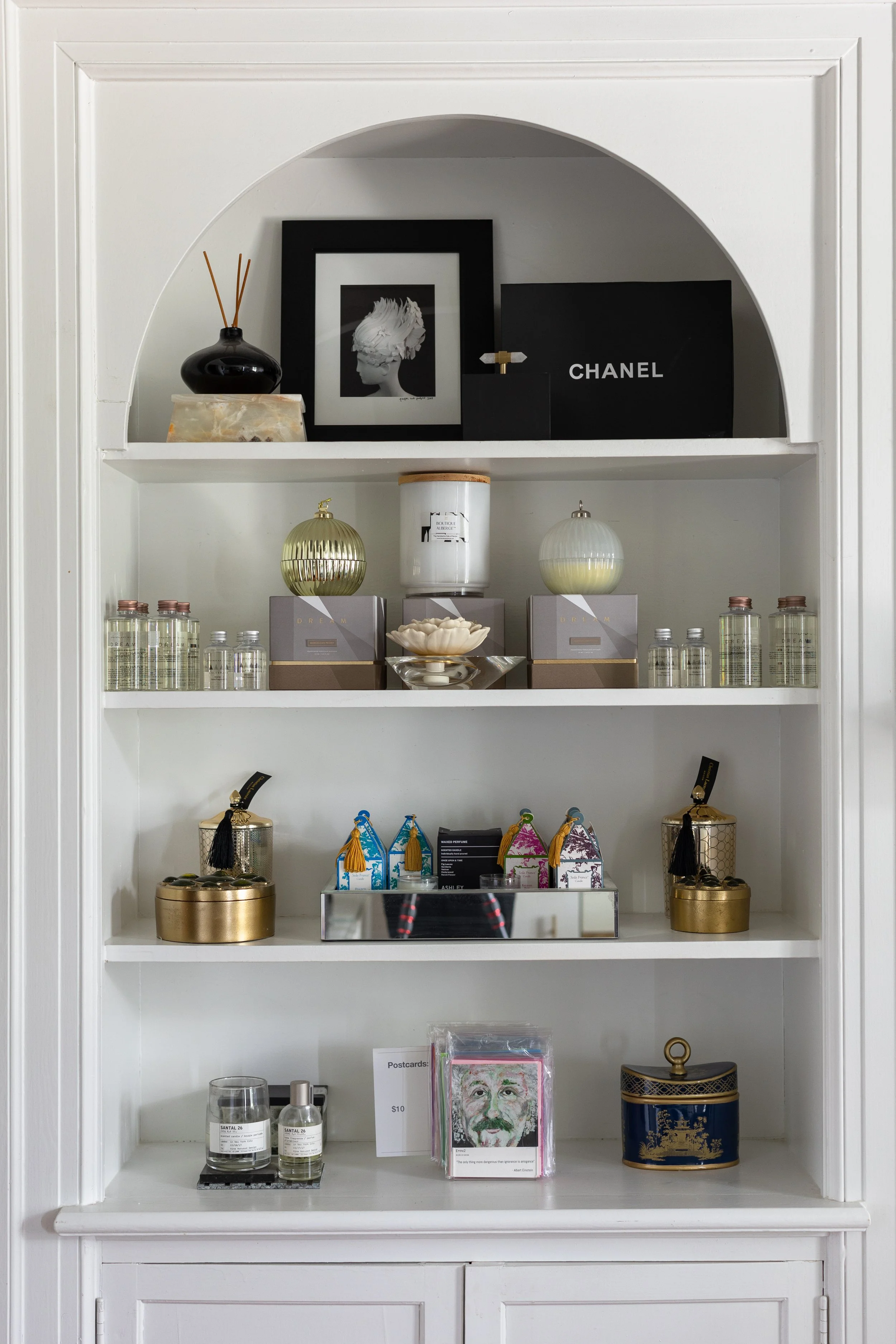 Decorative display shelf with framed art, perfume bottles, jewelry, small boxes, postcards, and decorative objects.