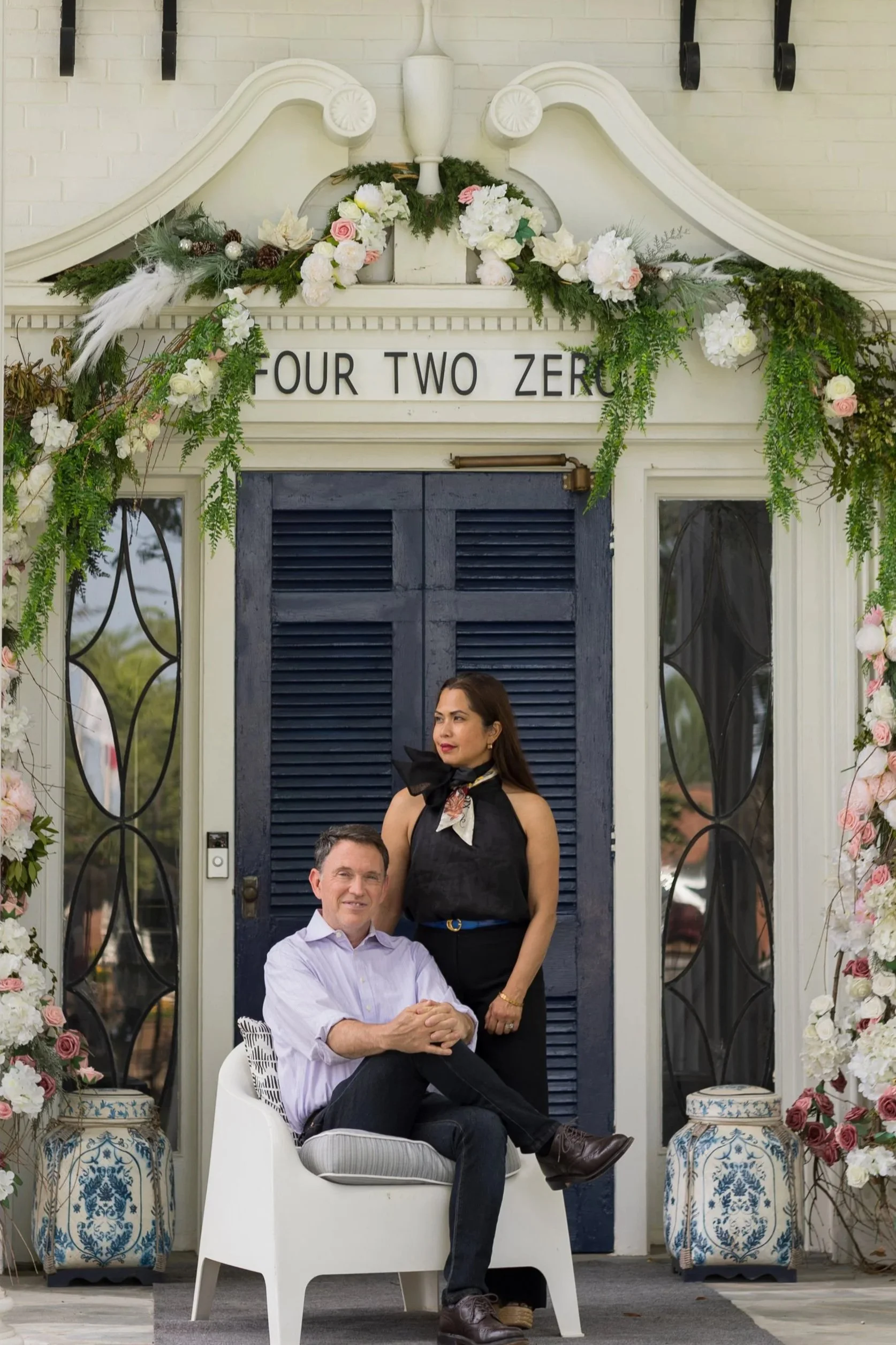 Arched floral backdrop stands Rina and Shan fairy godparents at Boutique auberge infront of an antique blue door