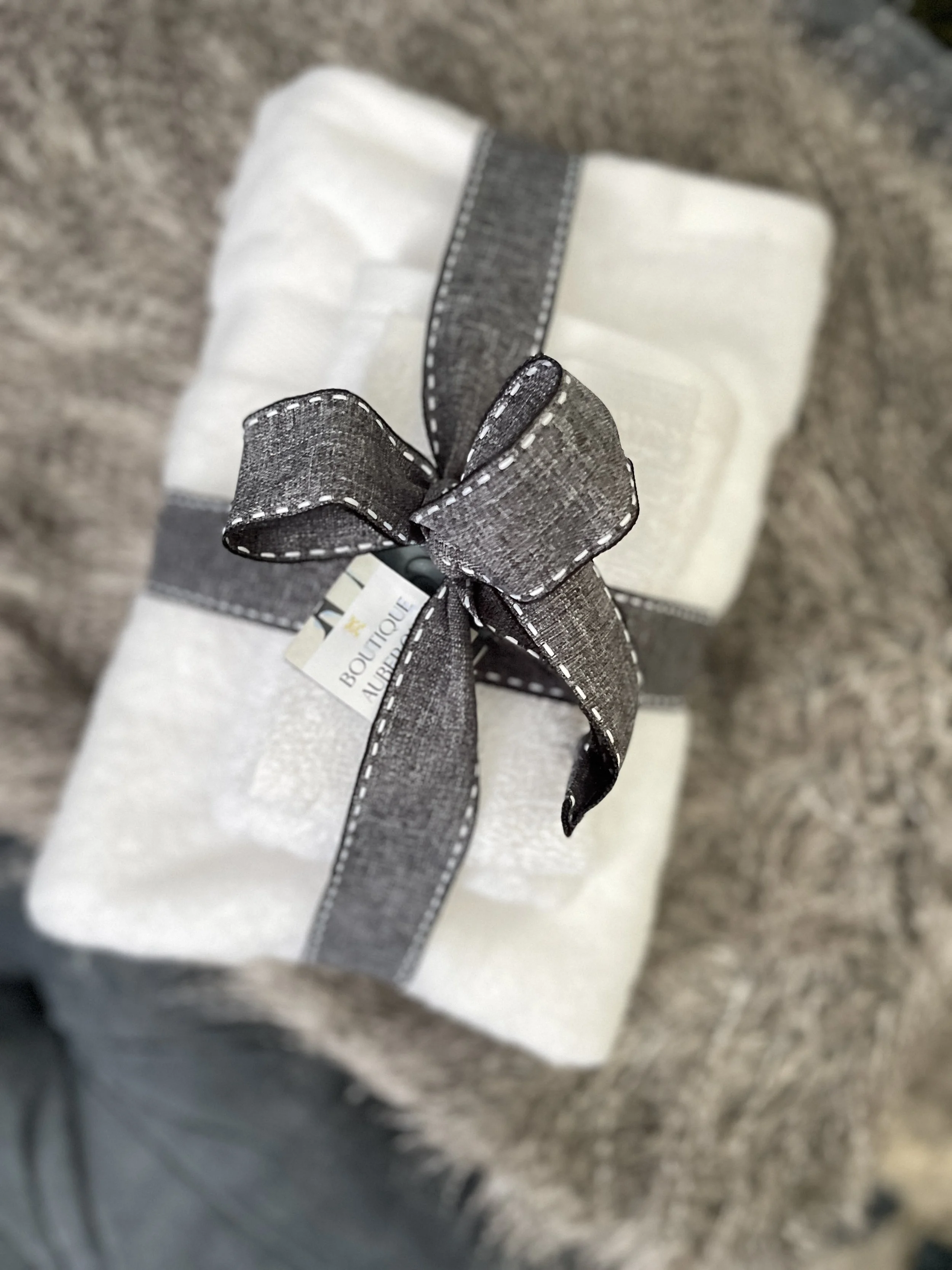 Wrapped gift box with a gray ribbon tied in a bow, placed on a furry surface.