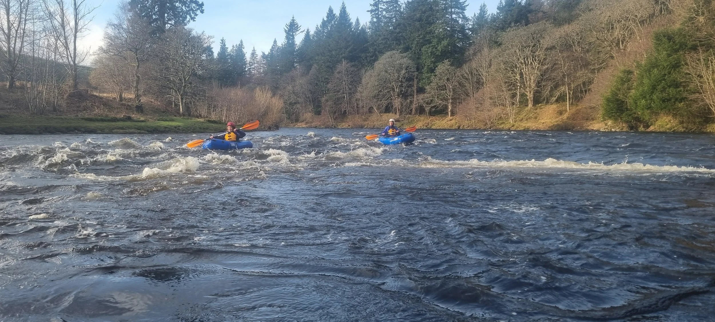 Two people kayaking on a river, surrounded by trees and a forested landscape.