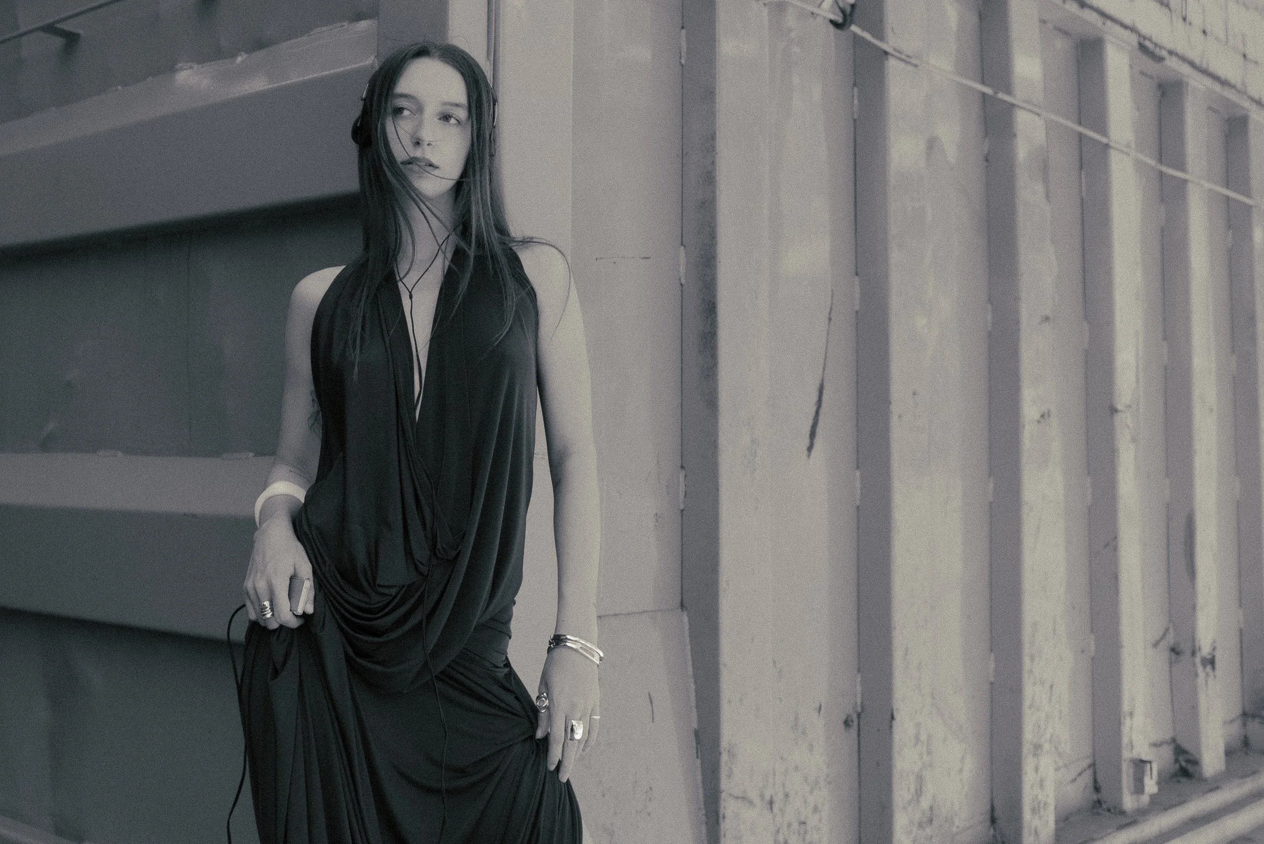 Une femme portant une robe noire et des écouteurs dans un environnement industriel avec des murs en béton.
