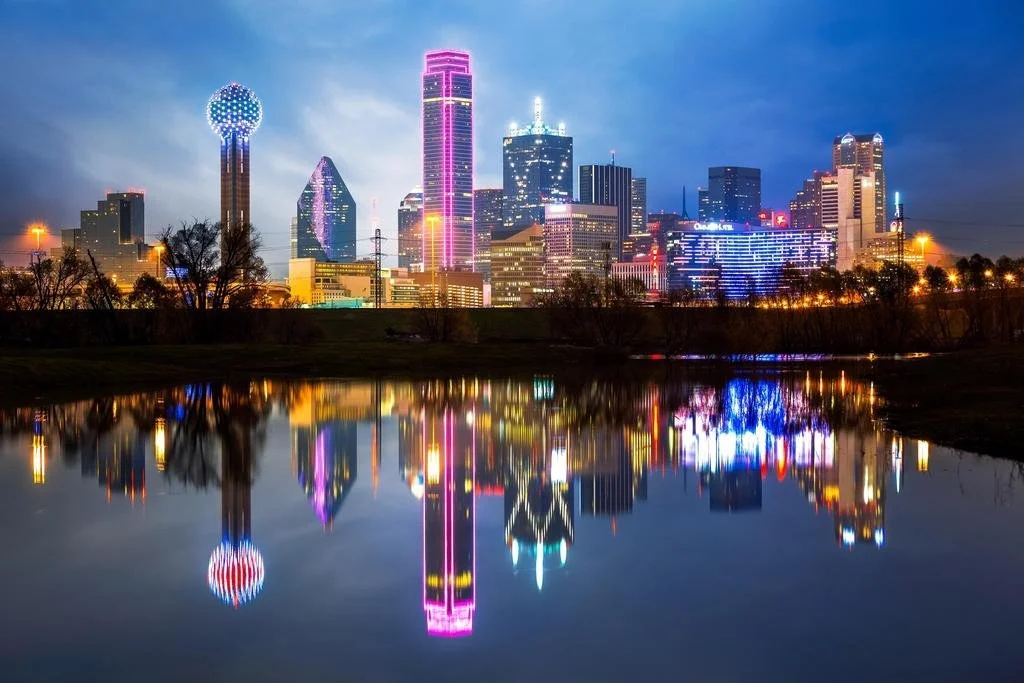 Dallas city skyline at night with colorful lit buildings reflecting on a calm body of water