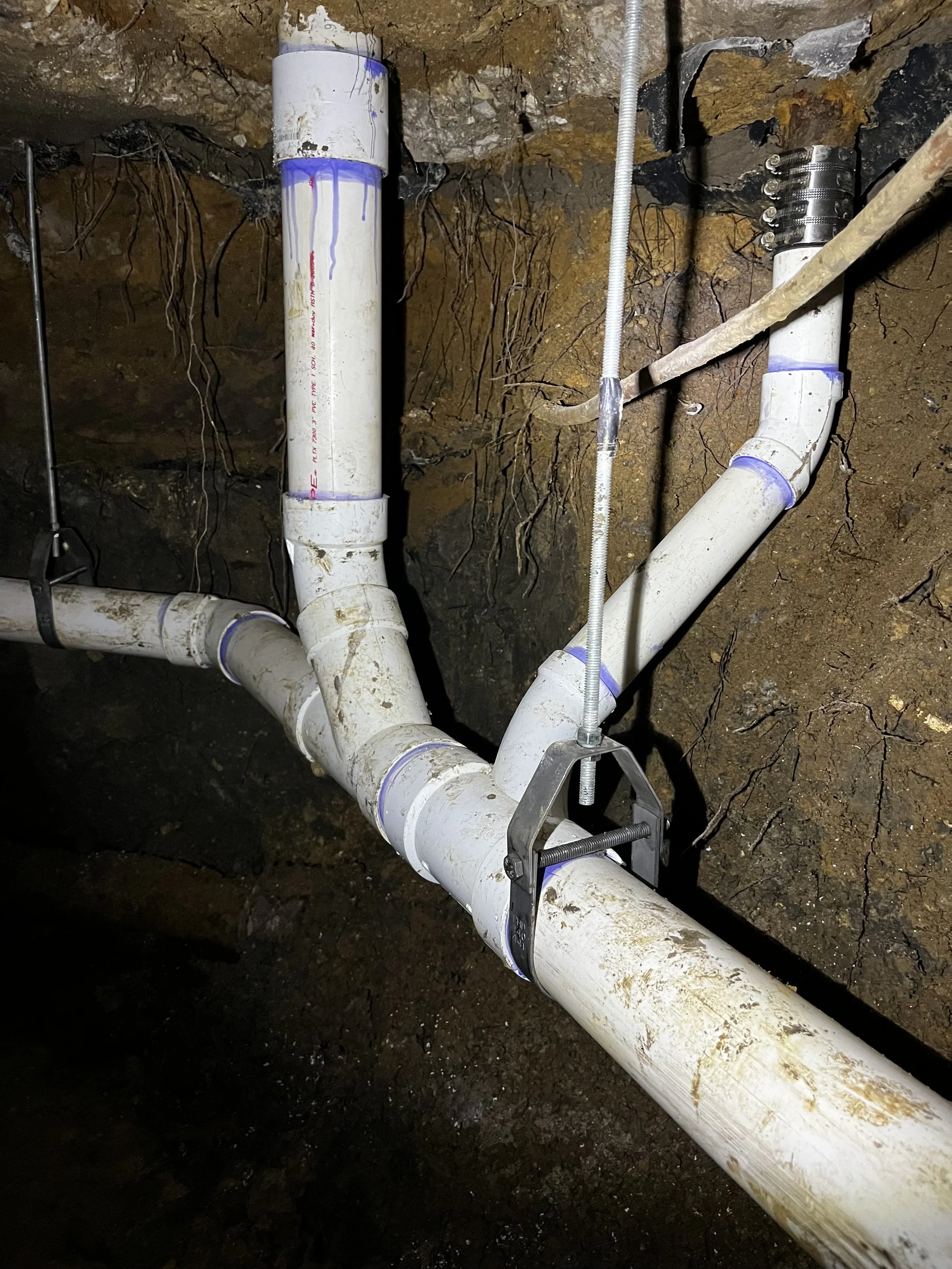 Underground plumbing pipes and fittings in a construction or repair site, with dirt and soil around.