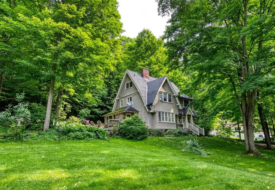 A large house with a steep roof is surrounded by lush green trees and a well-maintained lawn.