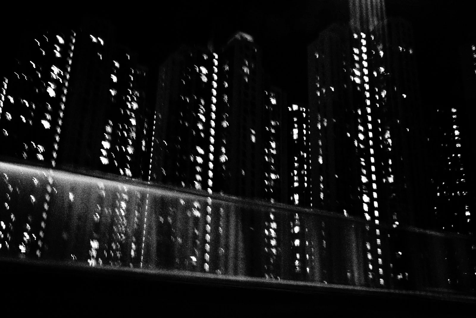 Nighttime cityscape with tall buildings and illuminated windows, black and white image.