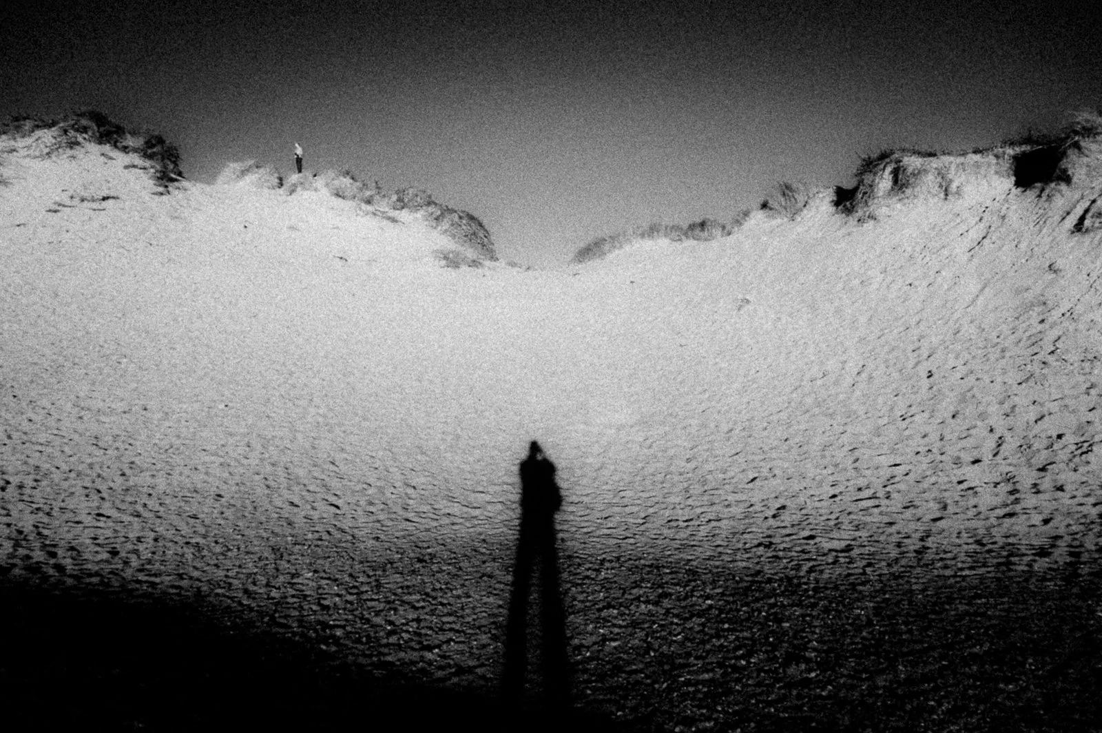 A silhouette of a person standing on a rocky beach with a large rock formation in the background, under a cloudy sky.