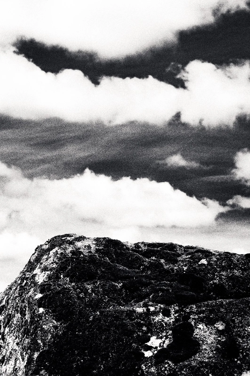 Black and white photo of a rugged mountain with a cloudy sky overhead.