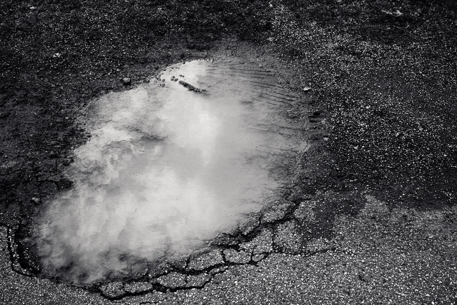 A large pothole filled with water on a cracked asphalt road.