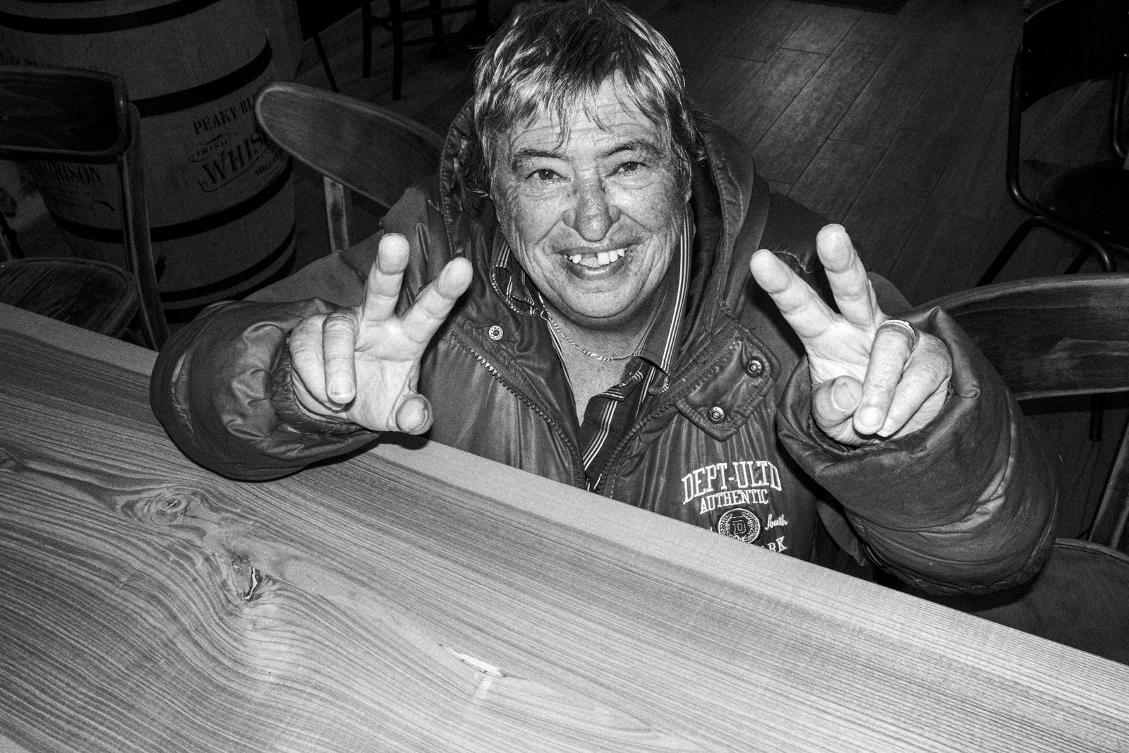 A smiling man with missing teeth making peace signs with both hands in a casual indoor setting.