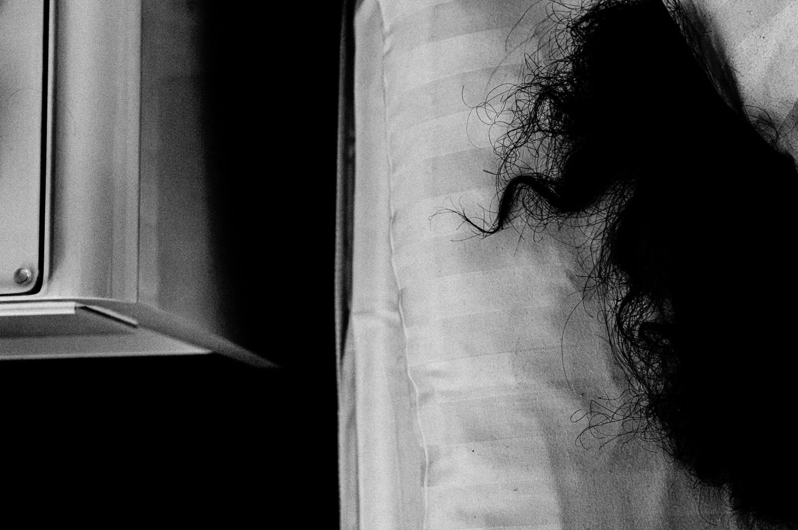 Close-up of a dark, curly hair on a white pillow next to a nightstand or cabinet.