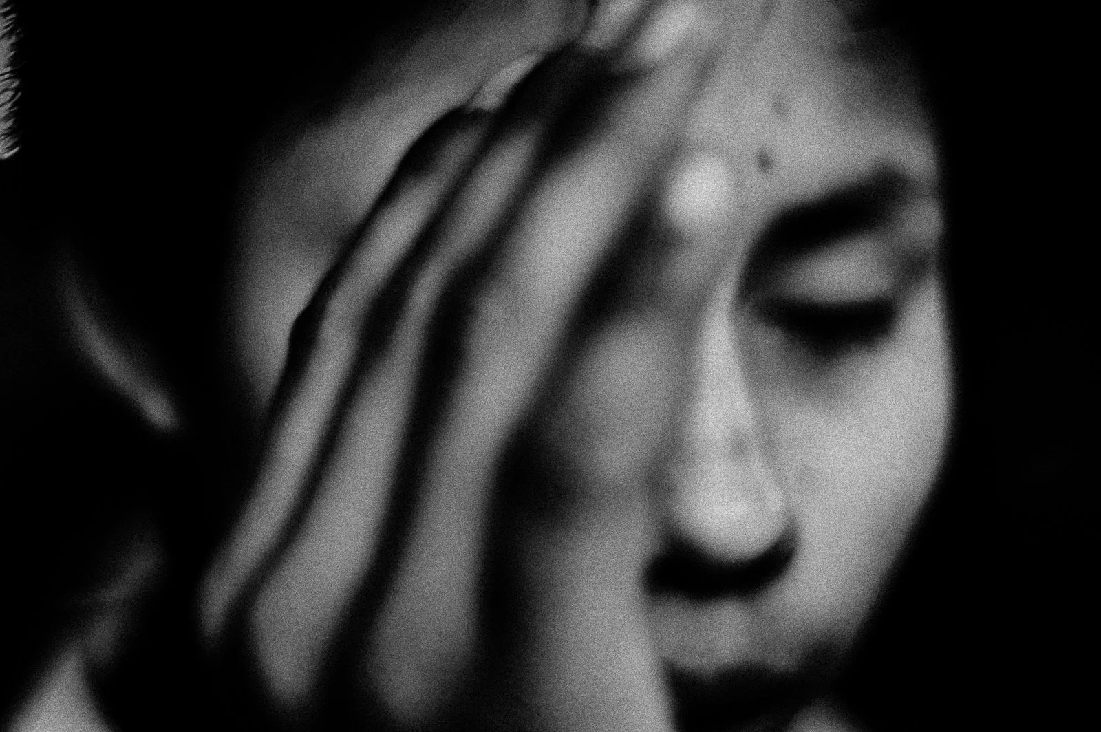 Close-up of a woman's face with her hand resting on her forehead, eyes closed, in black and white.
