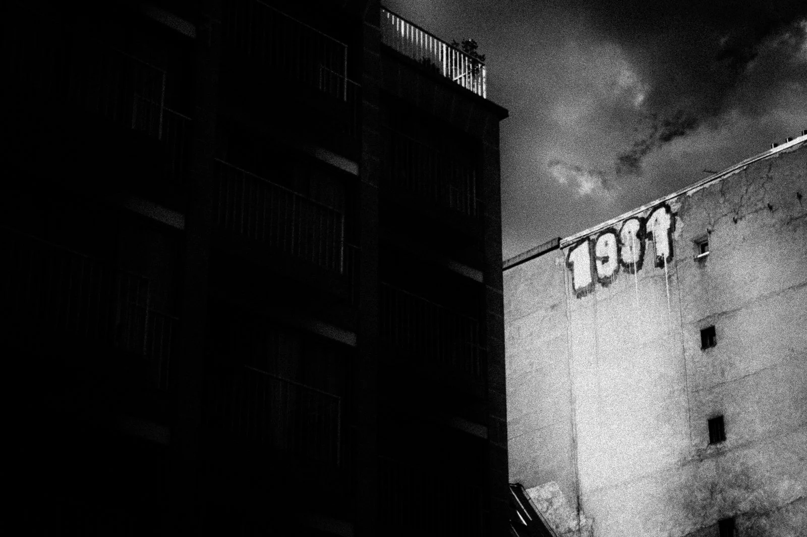 Black and white photo of two buildings, one with balconies and the other with a HOTEL sign on the roof, under a cloudy sky.